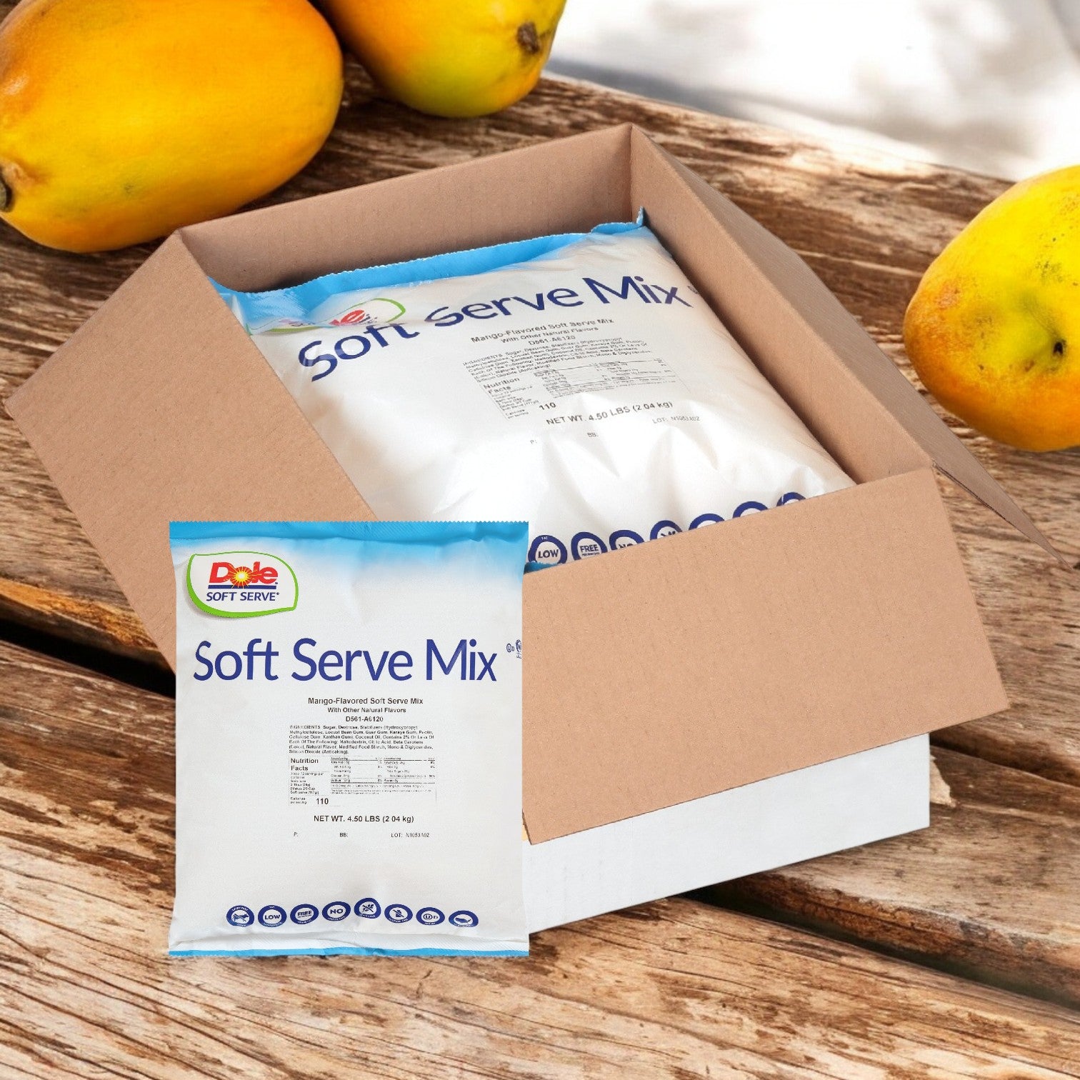 A box of Dole Soft Serve Mix Mango – 4 Bags (4.5 lbs Each) by Dole is displayed on a wooden surface, with fresh mangoes nearby to emphasize its real mango flavor.