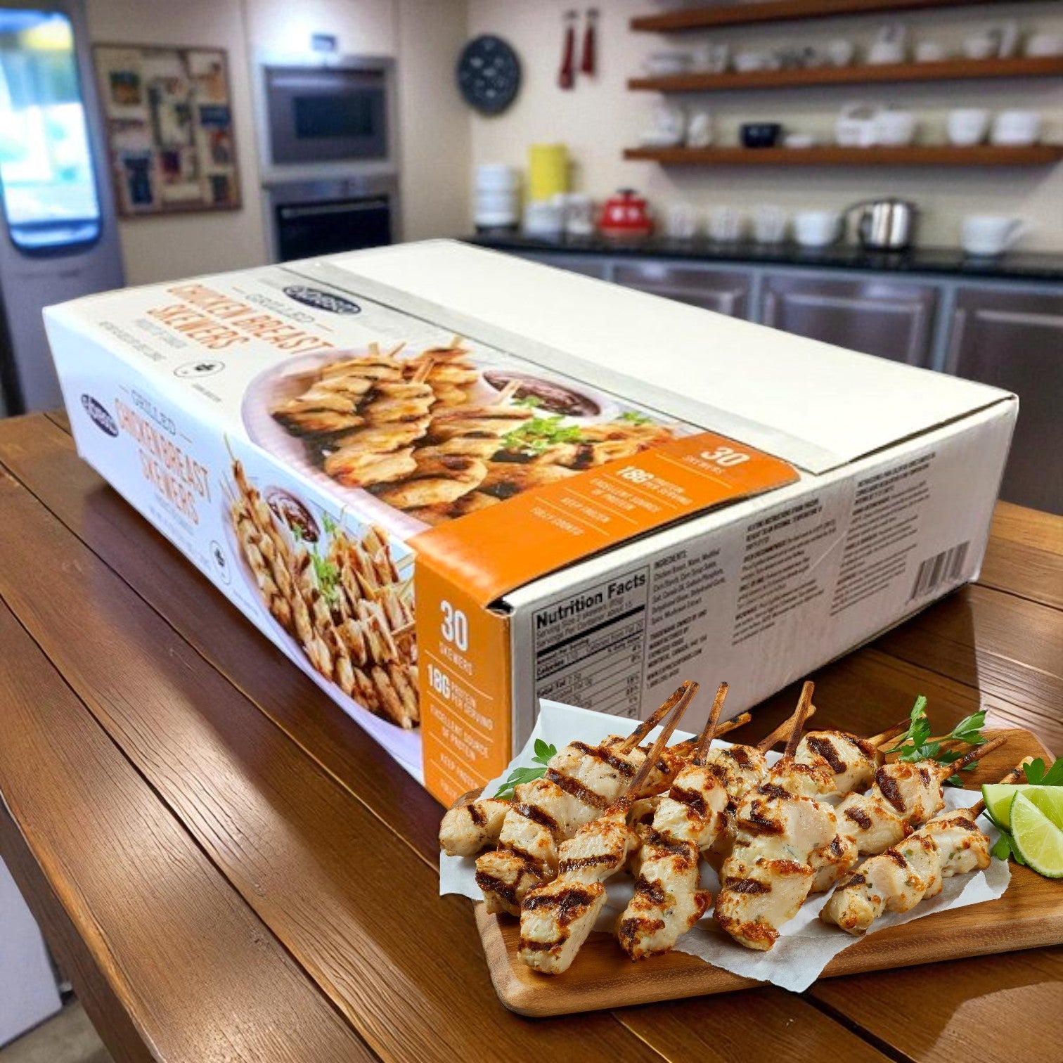 A large box of Gordon Choice Chicken Skewers sits on a wooden counter with a plate of grilled skewers in front; shelves and dishes in the kitchen background make it perfect for a high-protein snack.