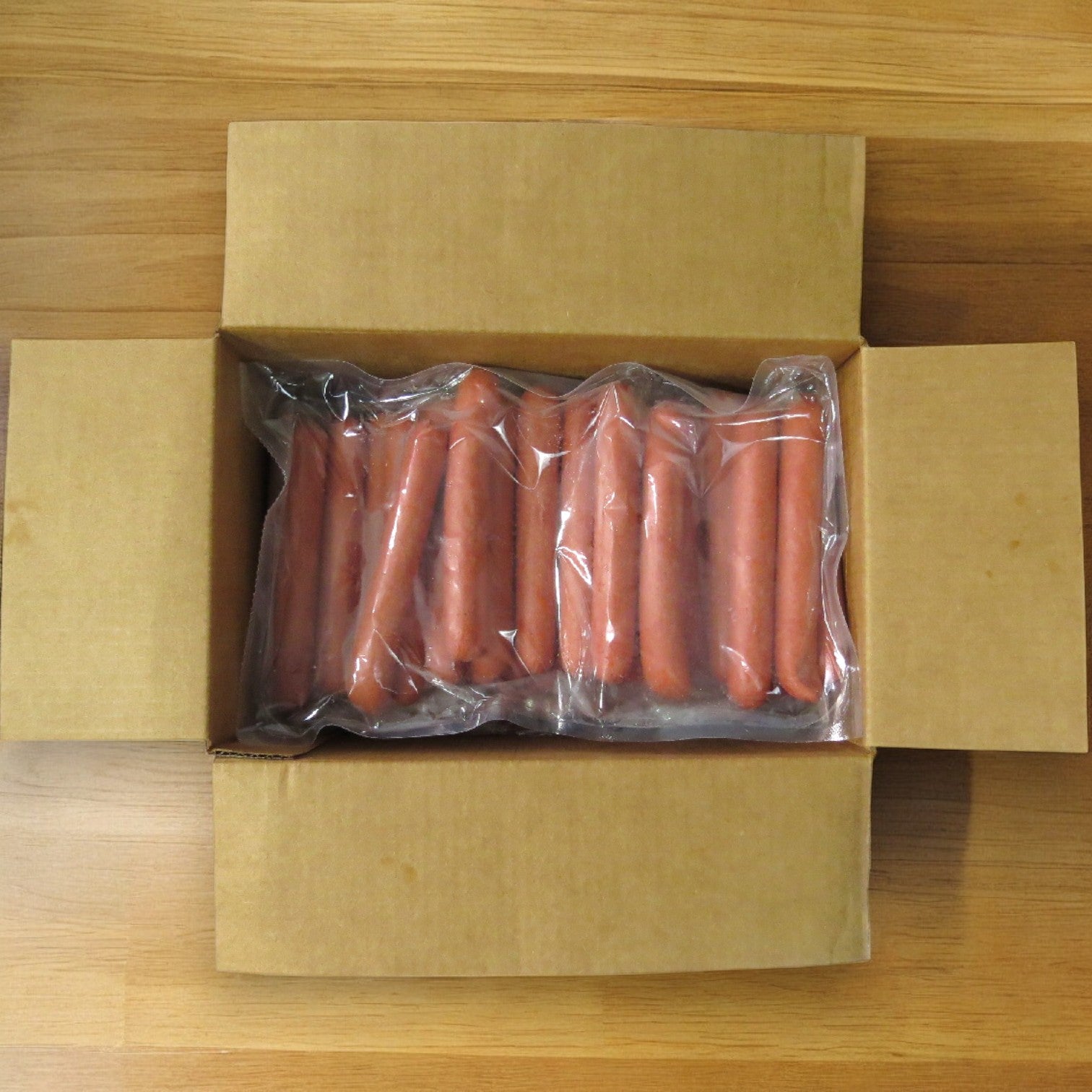 An open cardboard box of Vienna Beef Franks – 6" (6 hot dogs per lb., 60 total) shows two vacuum-sealed packs of all-beef hot dogs from Vienna Beef on a wooden surface.