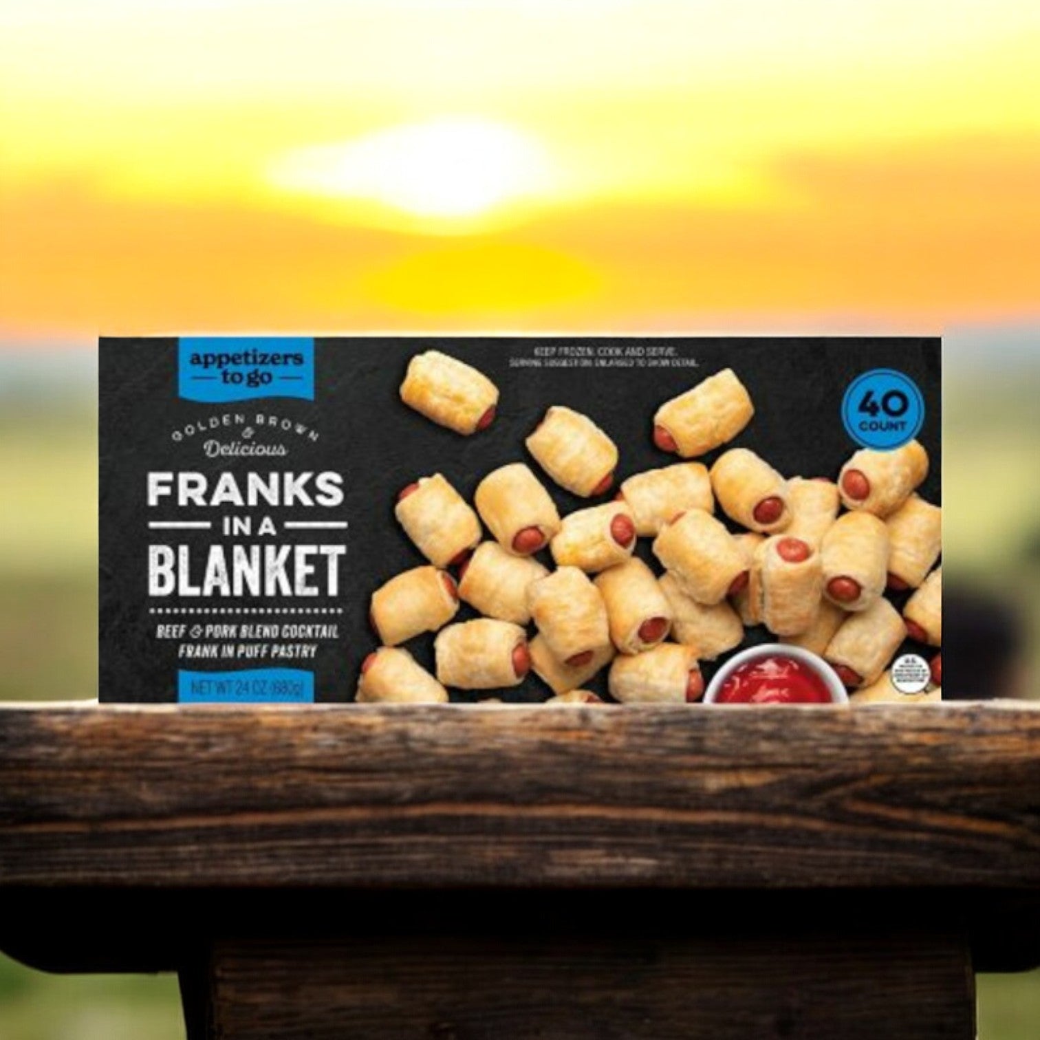 The "Franks In A Blanket Beef & Pork Blend" from Appetizers To Go features cocktail franks wrapped in puff pastry. This 40-count pack is shown on a wooden surface with a softly blurred backdrop.