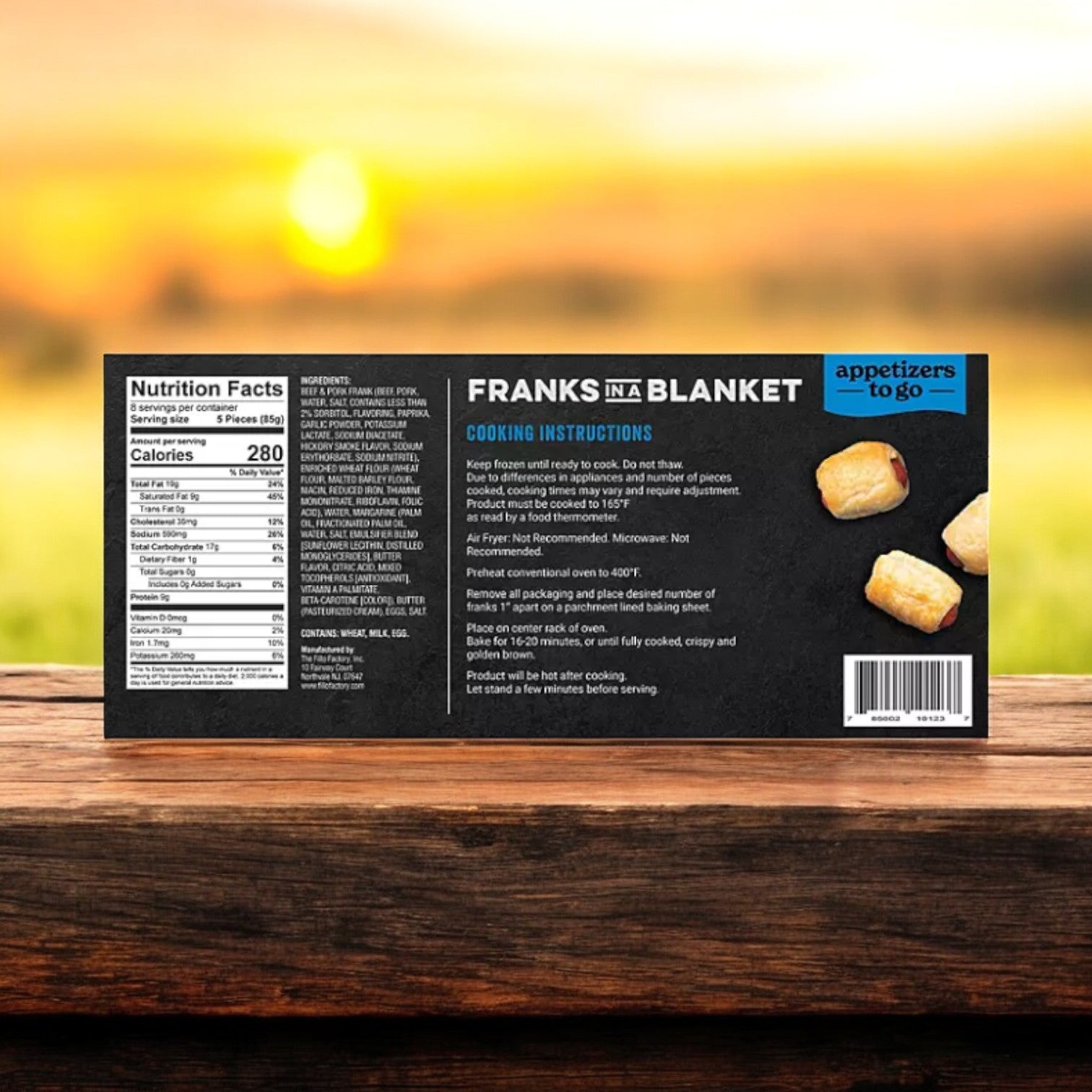 The Appetizers To Go packaging for "Franks In A Blanket Beef & Pork Blend Cocktail Frank In Puff Pastry, 40 Count - 3 Boxes" is set on a wooden surface. It displays nutritional info, ingredients, cooking instructions, and serving tips against a soft-focus outdoor backdrop.