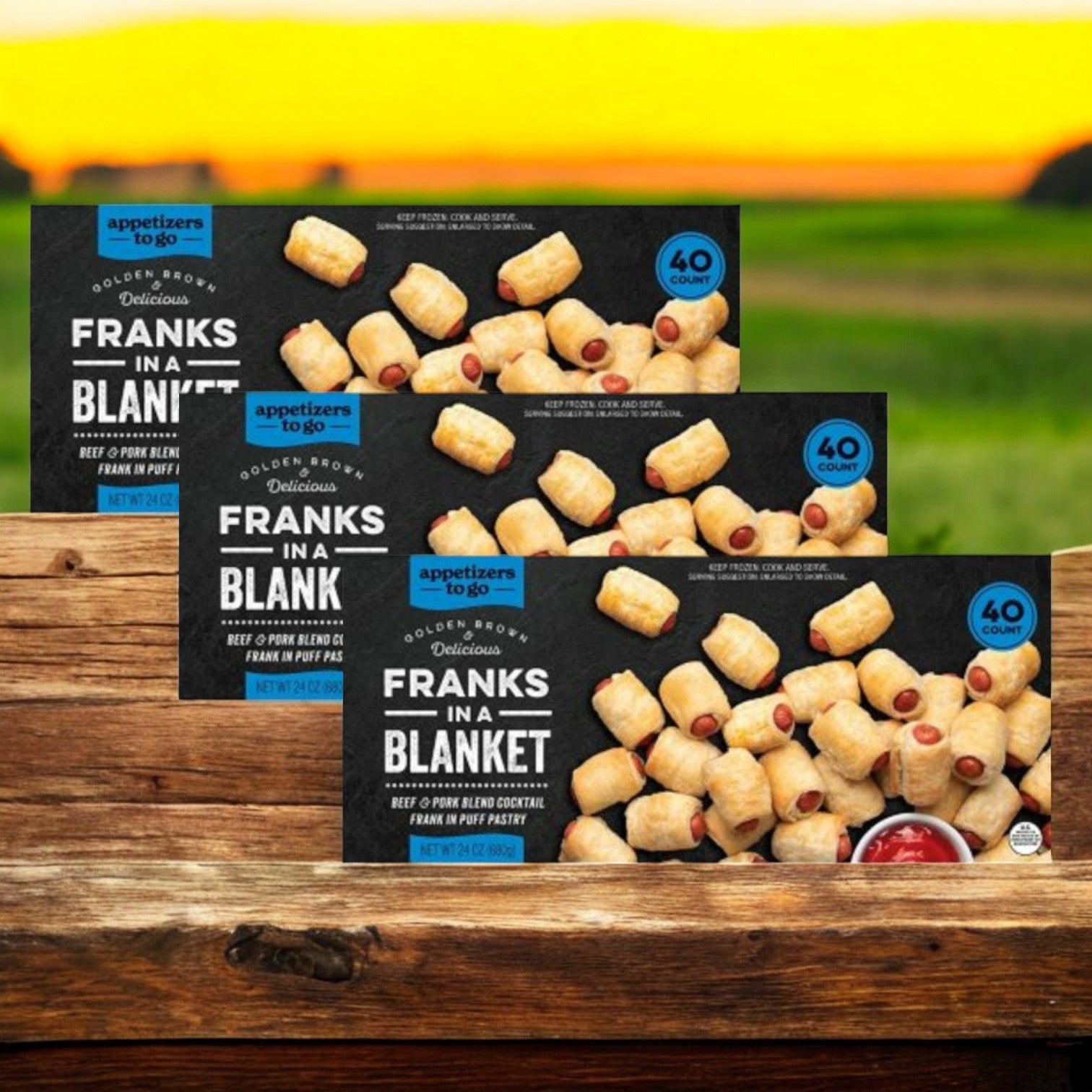 Three boxes of "Appetizers To Go's Franks In A Blanket" contain 40 beef and pork blend cocktail franks wrapped in flaky puff pastry, displayed against a scenic sunset.
