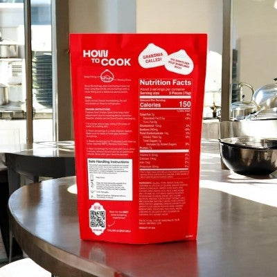 A MiLa Frozen Soup Dumplings - Pork - 1 Count package stands upright on a kitchen counter. The red Mila-branded pack shows cooking instructions and nutrition facts, promising authentic flavor, with kitchenware visible in the background.