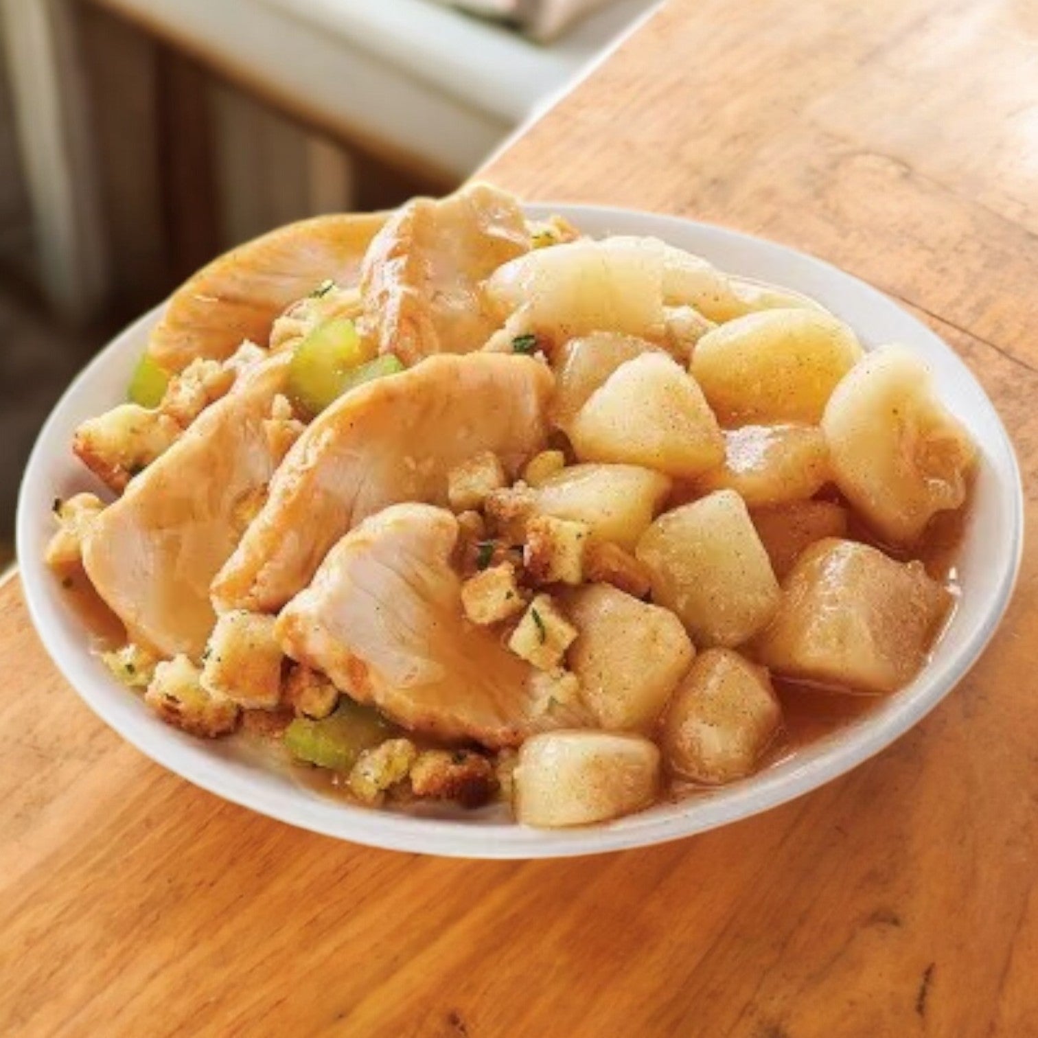 A bowl of Lean Cuisine Protein Kick Frozen Roasted Turkey Breast sits on a wooden table, featuring diced potatoes, stuffing, and brown gravy for a hearty meal.