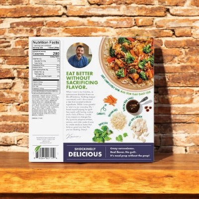 A box of Kevin's Natural Foods Korean BBQ-Style Chicken sits on a wooden surface, showing nutrition facts, a chef’s photo, and the message "Eat better without sacrificing flavor"—highlighting clean ingredients.