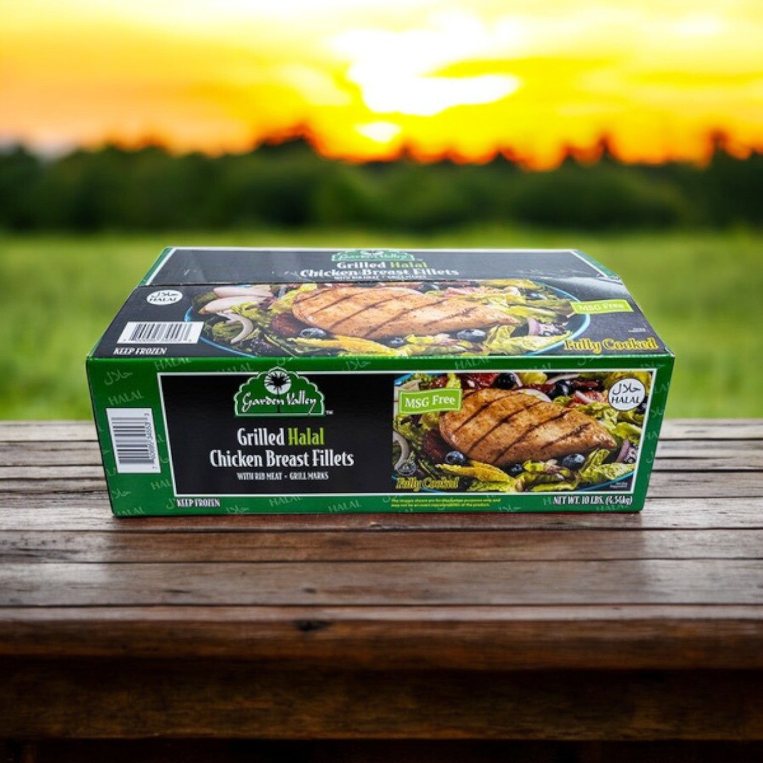A 10 lbs box of Restaurant Depot Grilled Halal Chicken Breast Fillets, Fully Cooked, rests on a wooden surface outdoors with a sunset and grassy field in the background.