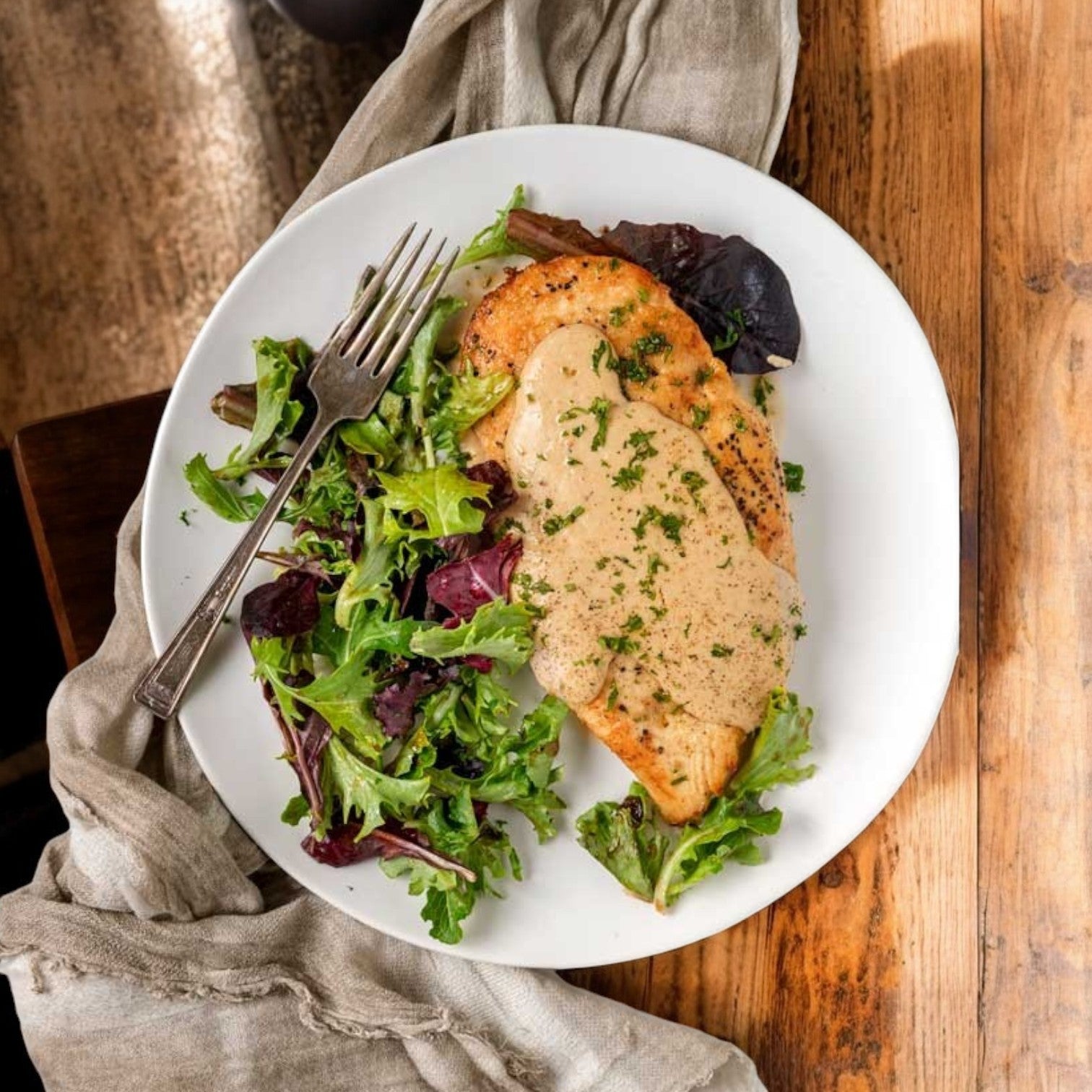 Restaurant Depot’s Grilled Halal Chicken Breast Fillets, Fully Cooked – 10 lbs, served with creamy sauce and mixed green salad. Ready to enjoy for your next meal—delicious and convenient on a wooden table setting.