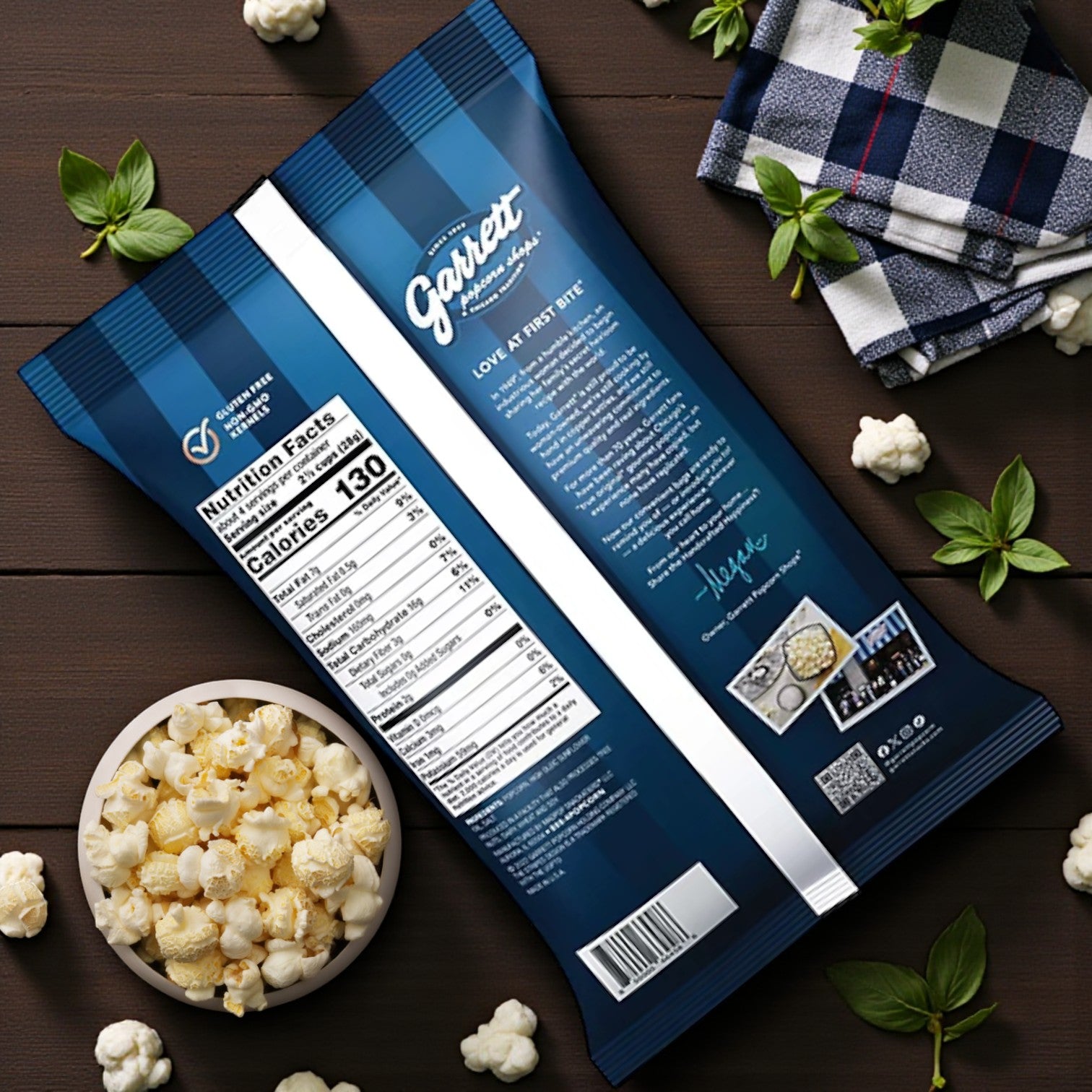 A 4 oz bag of Garrett Popcorn – Simply Salted by Garrett is displayed from the back next to a bowl of Simply Salted popcorn, small cauliflower pieces, herbs, and a checkered napkin on a wooden surface.