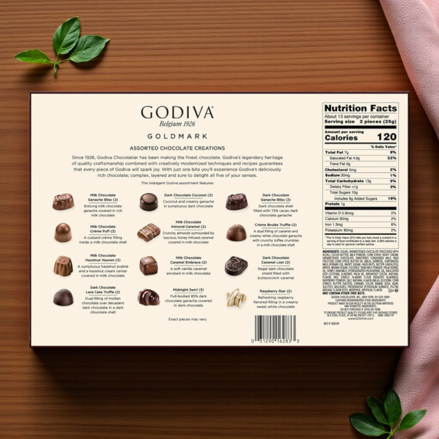 Back of a Godiva Premium Assorted Chocolates – 27 Count box shows Belgian chocolate details and nutrition facts, with a pink fabric in the corner, on a wooden surface.