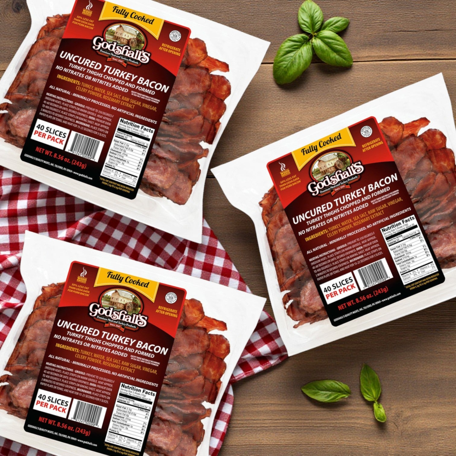 Three packs of Godshall's Uncured Fully-Cooked Turkey (40 oz each) are displayed on a wooden surface with basil leaves and a red checkered cloth.