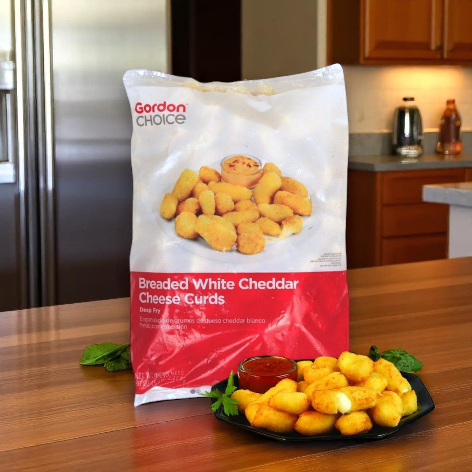An 80 oz bag of Easy Lunches Gordon Choice Breaded White Cheddar Cheese Curds is on a kitchen counter beside a black plate of white cheddar cheese curds and a small cup of dipping sauce.