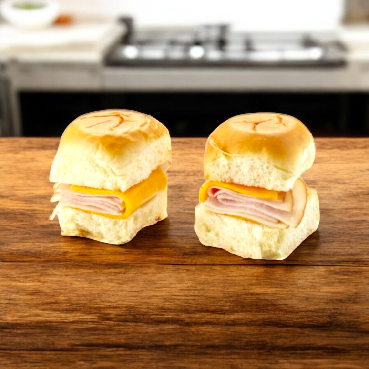 Two E.A. Sween Smoked White Turkey and Cheddar Sliders with cheese on mini buns sit on a wooden surface, encompassed by a cozy kitchen ambiance.