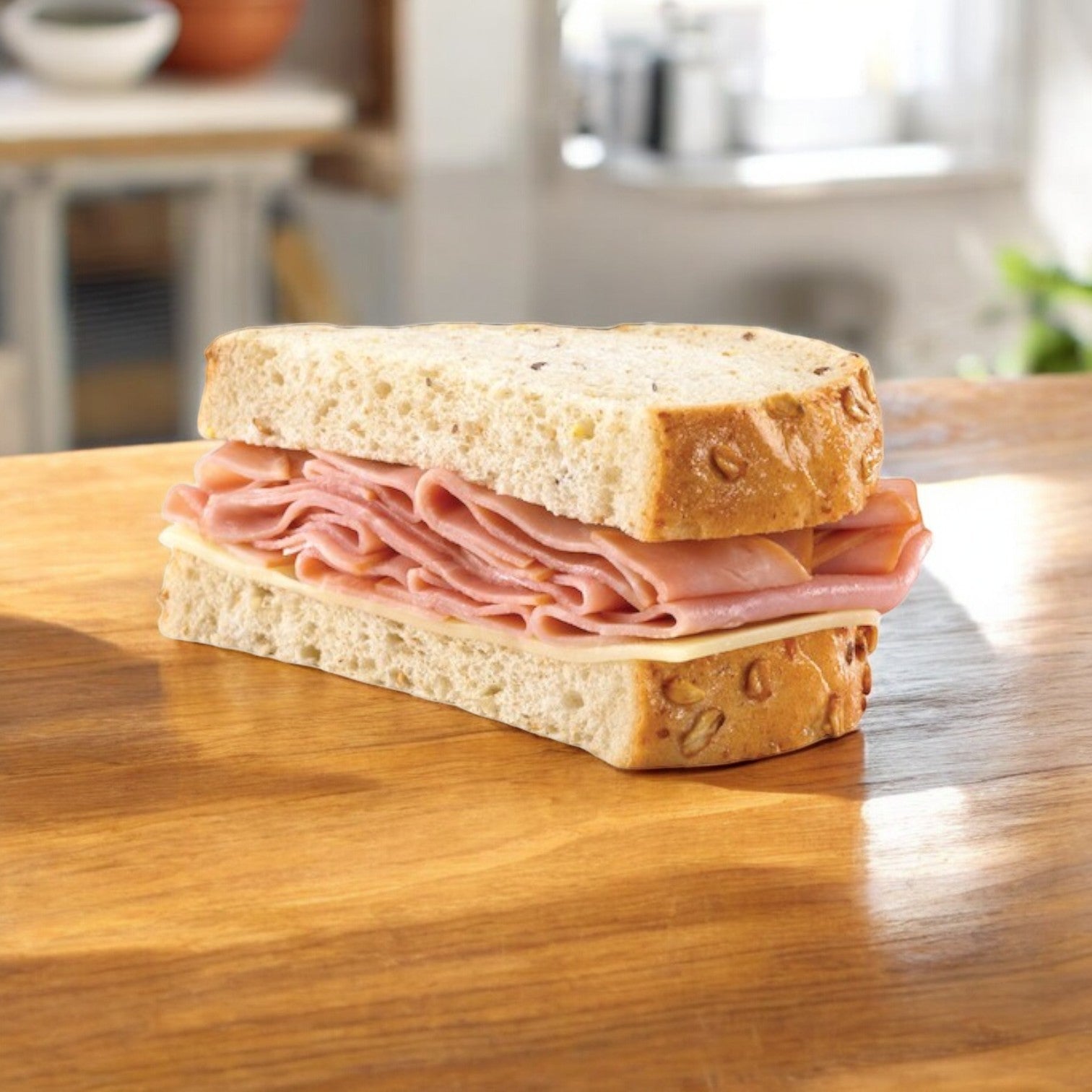 A Ham & Swiss sandwich from E.A. Sween, featuring premium ham and cheese on oat-topped wheat bread, sits on a wooden surface.