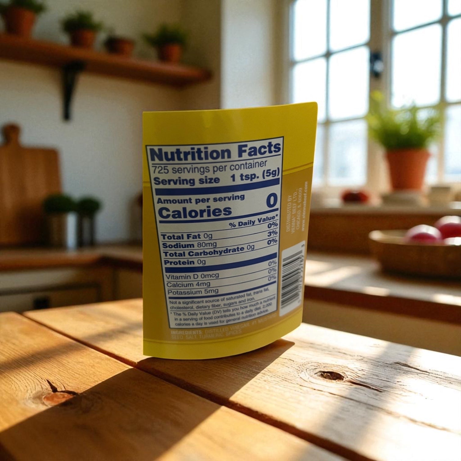 A Vienna Beef Vienna Yellow Mustard 1 Gallon Jar with nutrition facts is on a wooden kitchen table; potted plants and fruit are visible in the sunlit background.