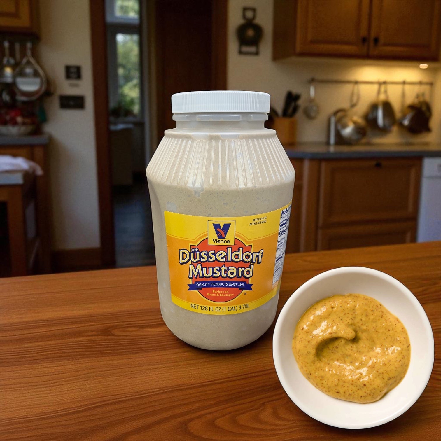 A 1-gallon jar of Easy Lunches Vienna Dusseldorf Mustard rests on a kitchen counter beside a small white bowl filled with this gluten-free mustard.