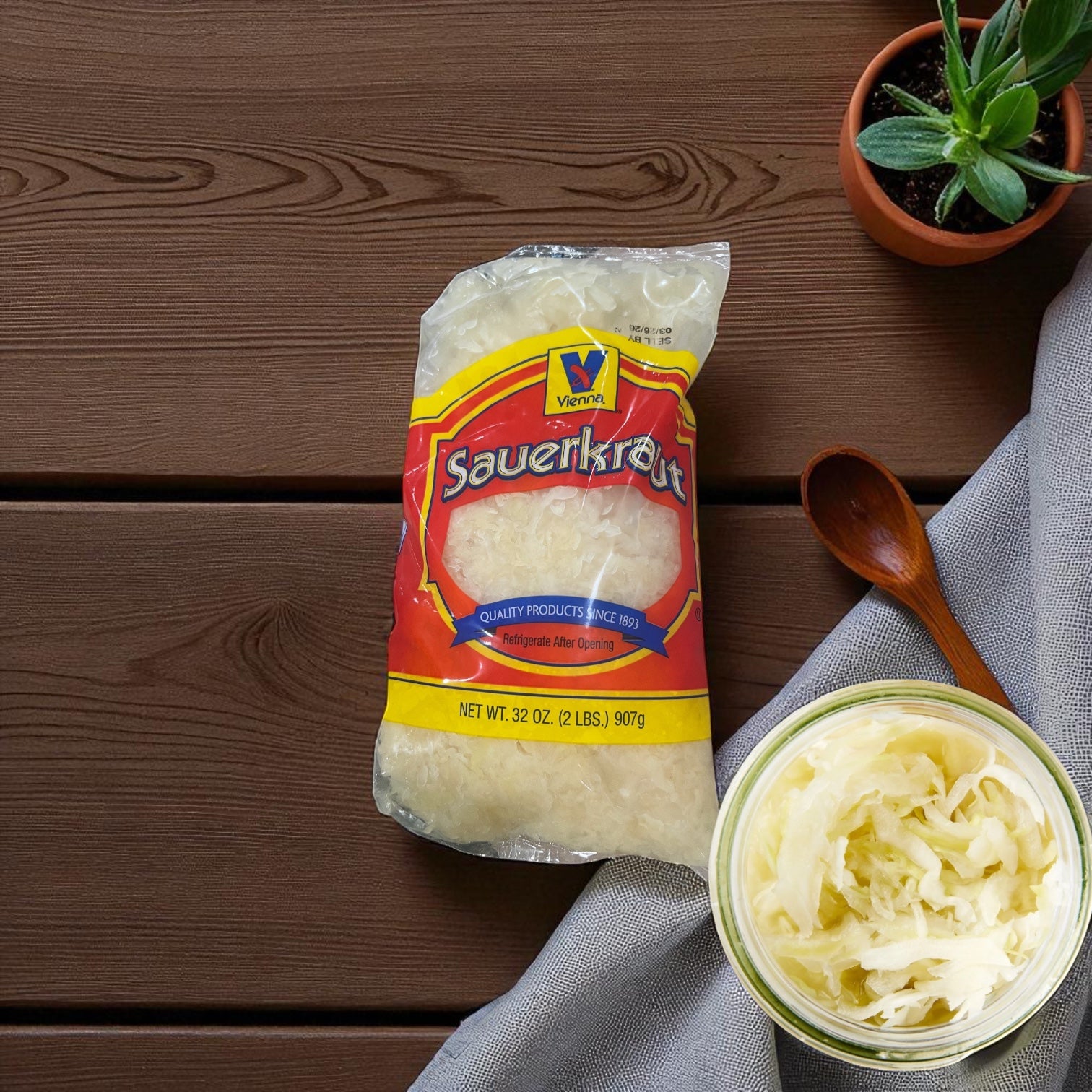A sealed bag of Vienna Beef Sauerkraut sits on a wooden table beside a potted plant, wooden spoon, and a sauerkraut jar—tasty sides for Vienna Beef or Chicago-style green relish.