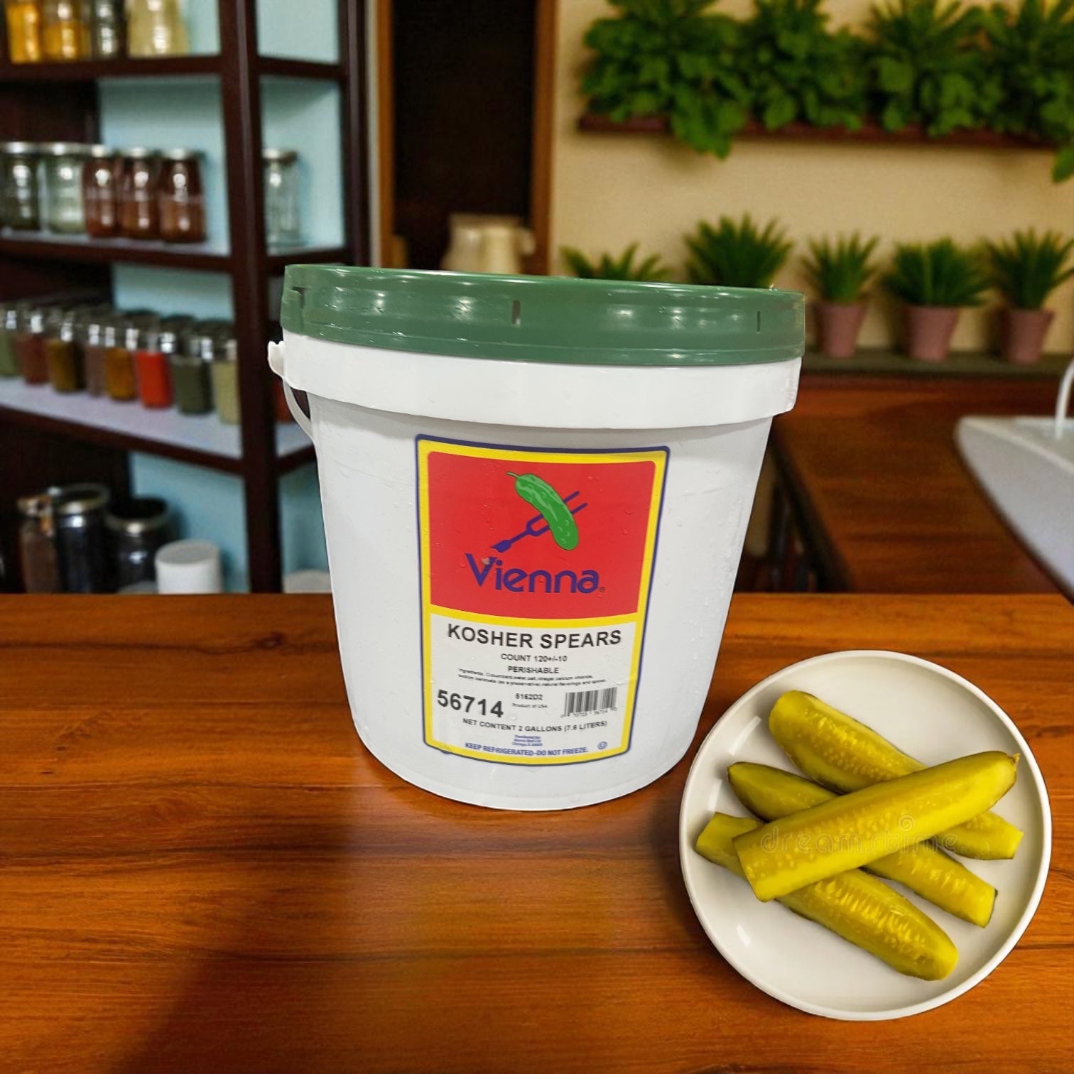 A large Vienna Beef Kosher Dill Spears 2 Gallon Jar sits on a wooden counter beside a plate of crunchy dill spears, with shelves of jars and potted plants in the background enhancing the kosher pickles display.