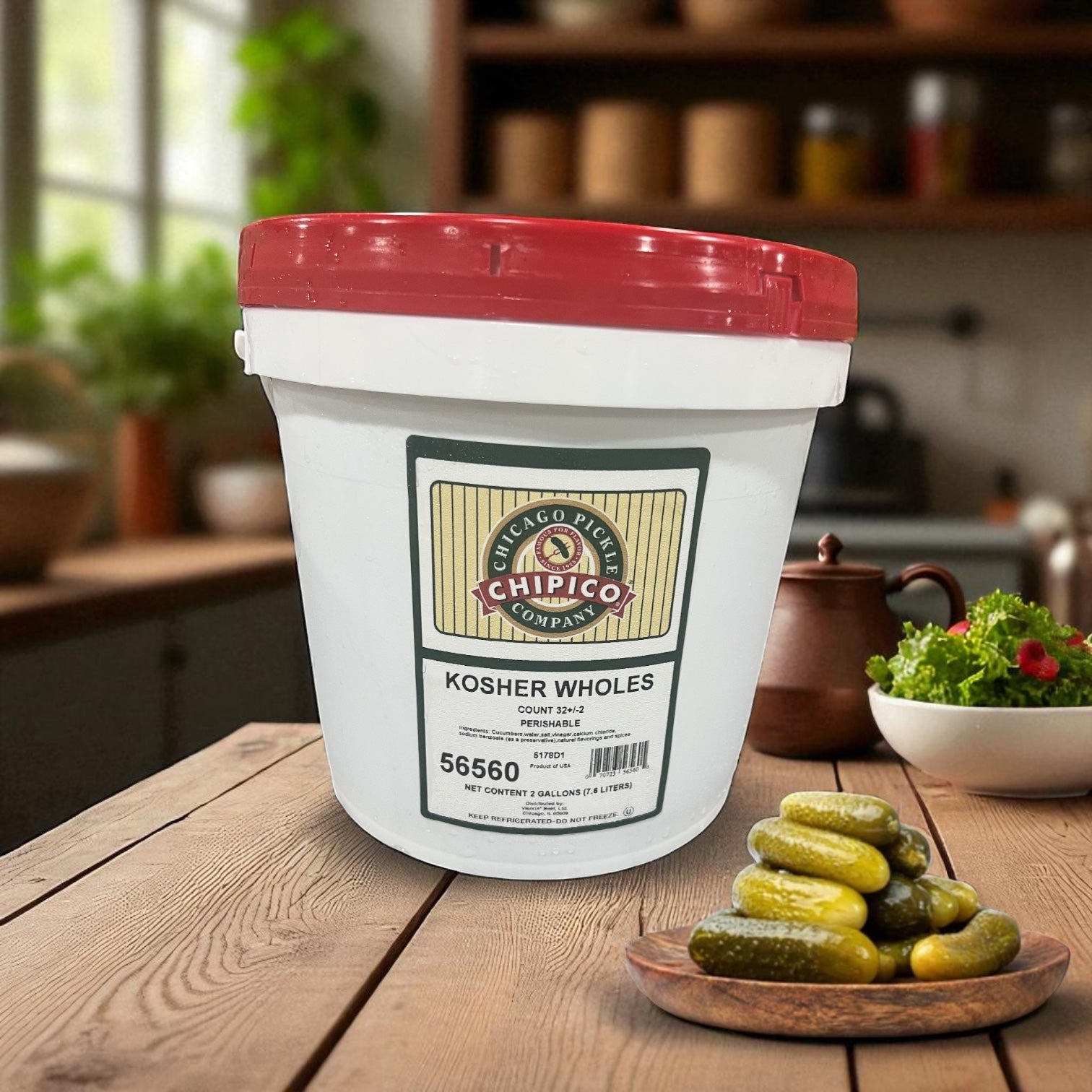 A 2-gallon Vienna Beef Chipico Kosher Wholes container sits on a kitchen counter next to a bowl of pickles, with a teapot and kitchen items in the background—ideal for foodservice pickle lovers.