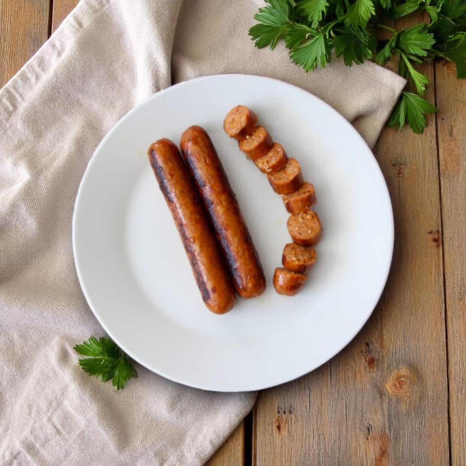 A white plate holds two whole and one sliced Vienna Beef Skinless Polish Sausage 6” 4:1, featuring traditional Polish flavor, on a beige napkin atop a wooden table and garnished with fresh parsley.