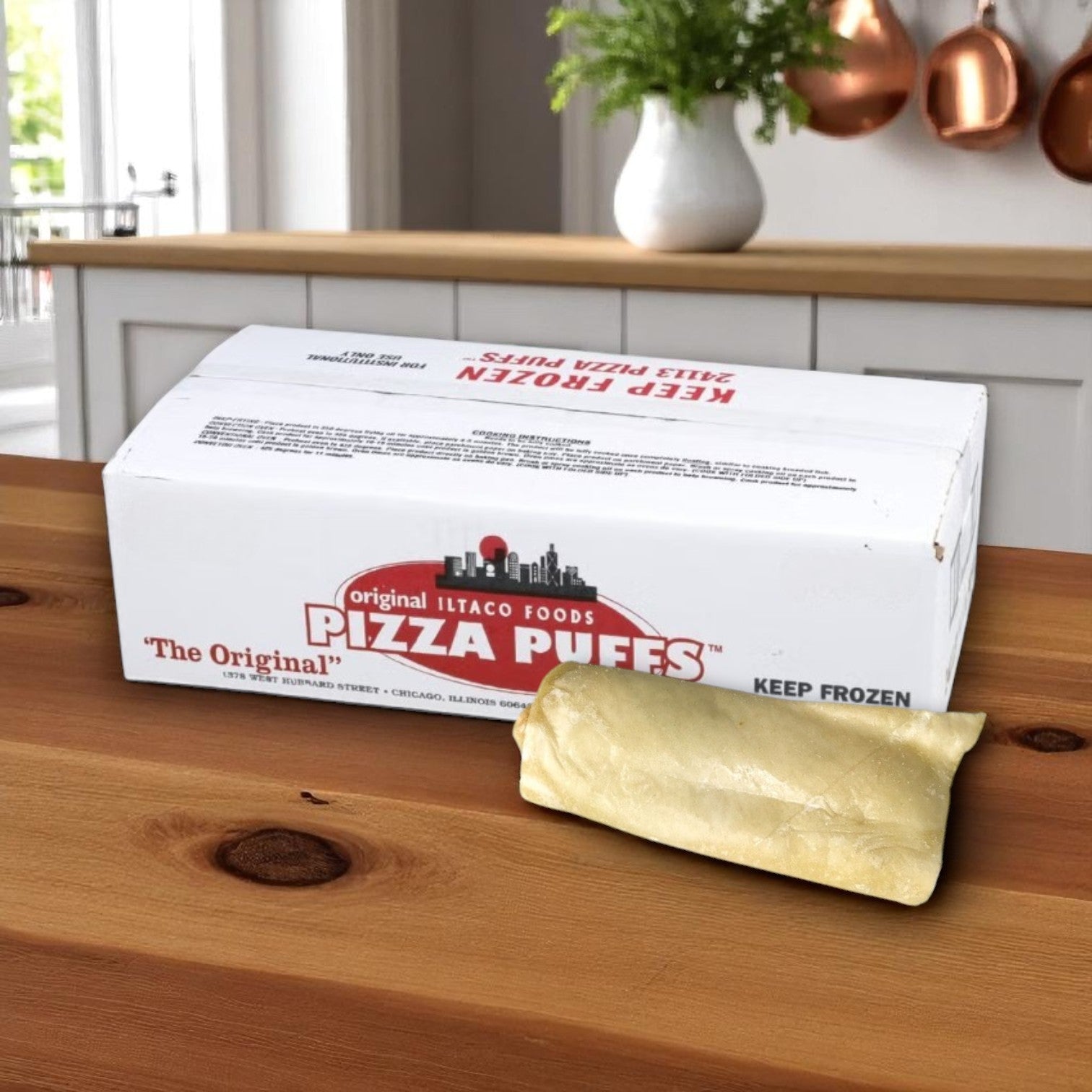 A box labeled "Iltaco Beef & Bean Burrito – 5 oz (48 per Case)" from The Original Pizza Puff sits on a kitchen counter, with one uncooked, individually wrapped burrito placed beside it.
