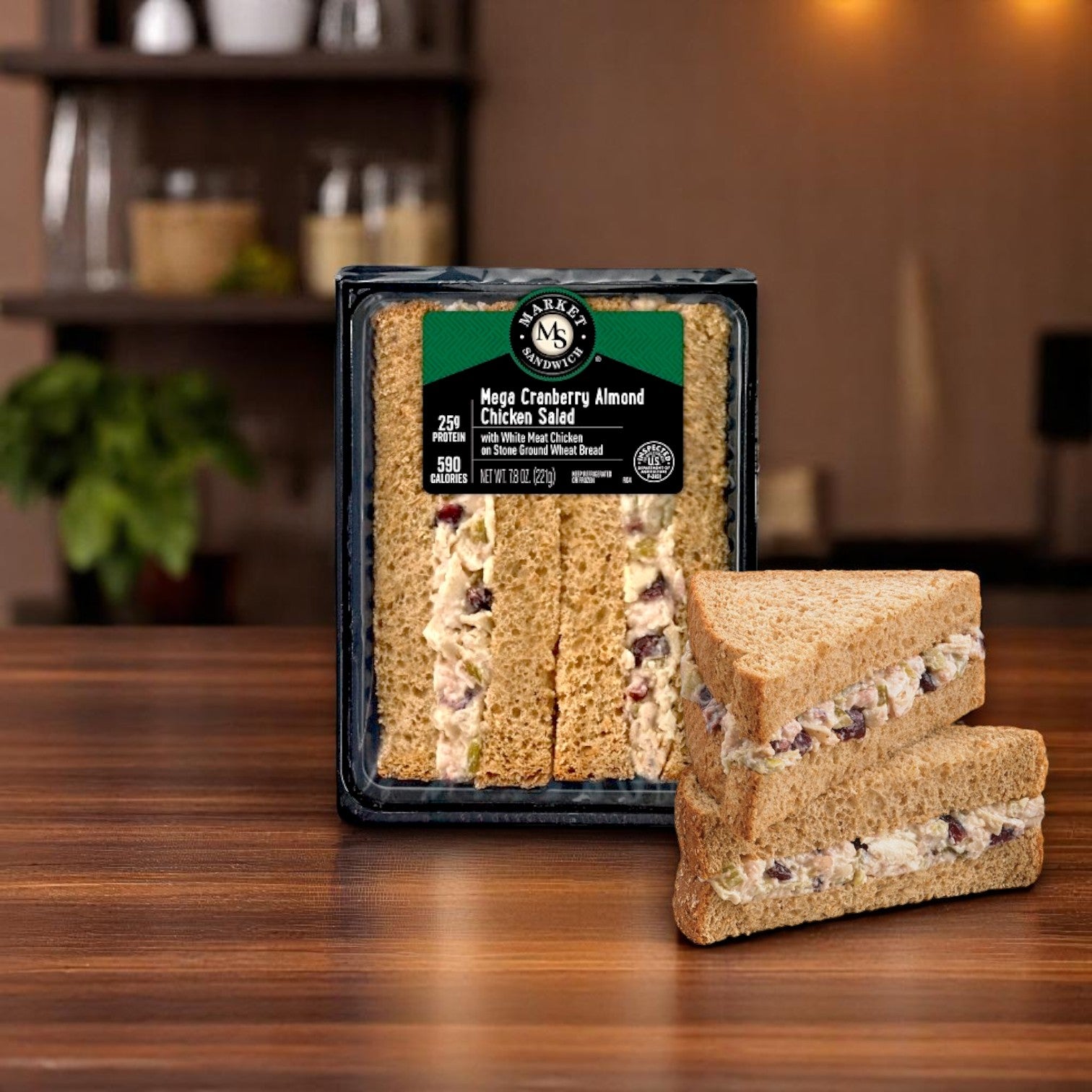 A Market Sandwich Mega Cranberry Almond Chicken Salad on Stone Ground Wheat Bread – 7.8 oz (Individually Wrapped) from E.A. Sween sits on a table, with two individually wrapped sandwich halves stacked in front of the package.