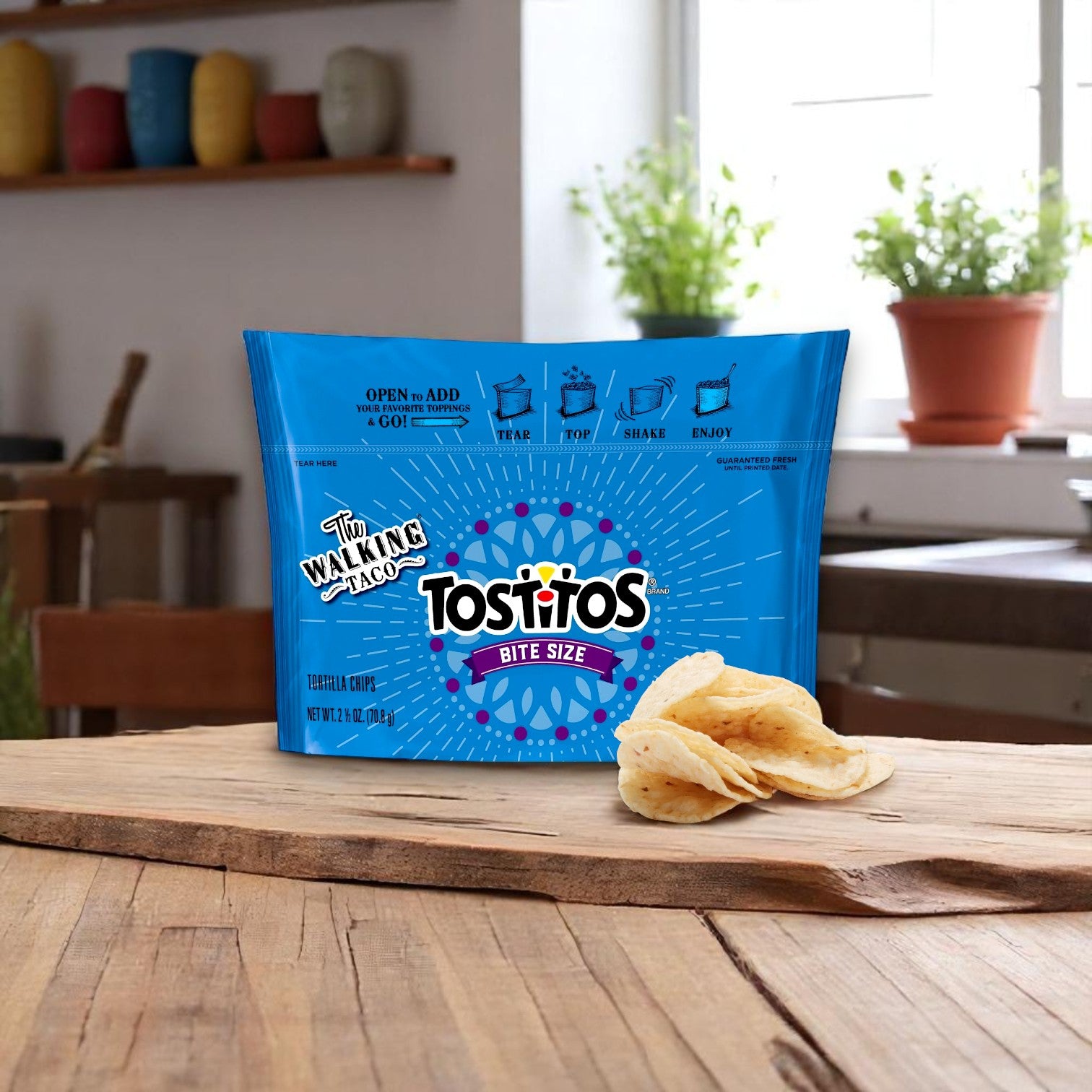 An 18-pack of Tostitos® Tortilla Chips Rounds (2.5 oz bags) sits on a wooden table with a stack of chips in front, ideal for dippable snacking delight; a kitchen with plants can be seen in the background.