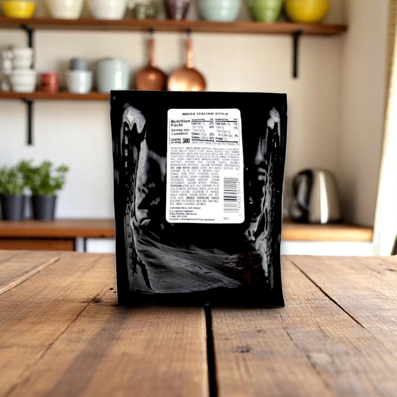 A black package labeled E.A. Sween Deli Express Mega Italian Style Sandwich Wedge – 5.7 oz, with a nutrition label, sits on a wooden table in a kitchen with shelves displaying cups and bowls in the background.