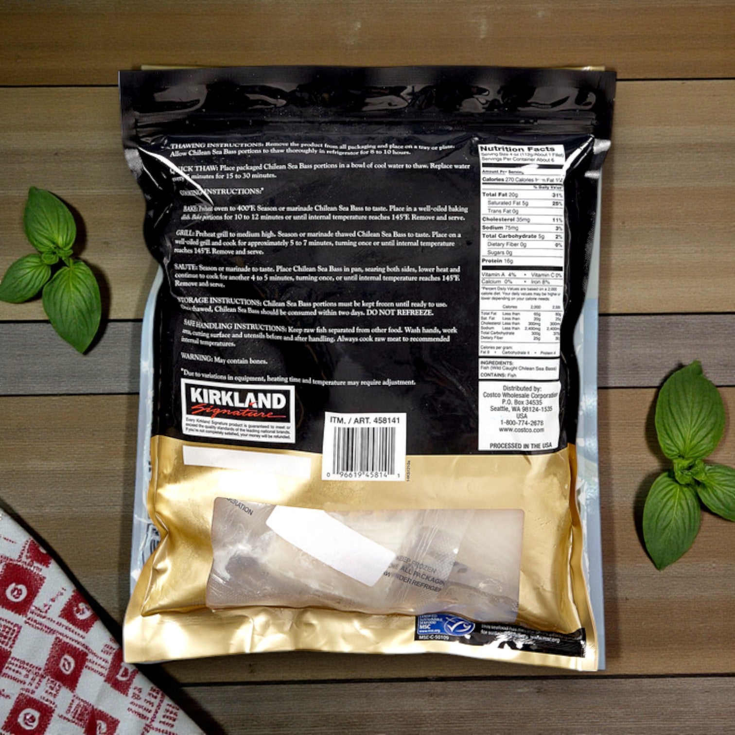 Back of a Kirkland Signature Wild Chilean Sea Bass bag (4–6 oz portions, 1.5 lbs), shows product info, cooking instructions, nutrition facts, and contact details on a wooden surface with herbs—similar to premium fish packaging.