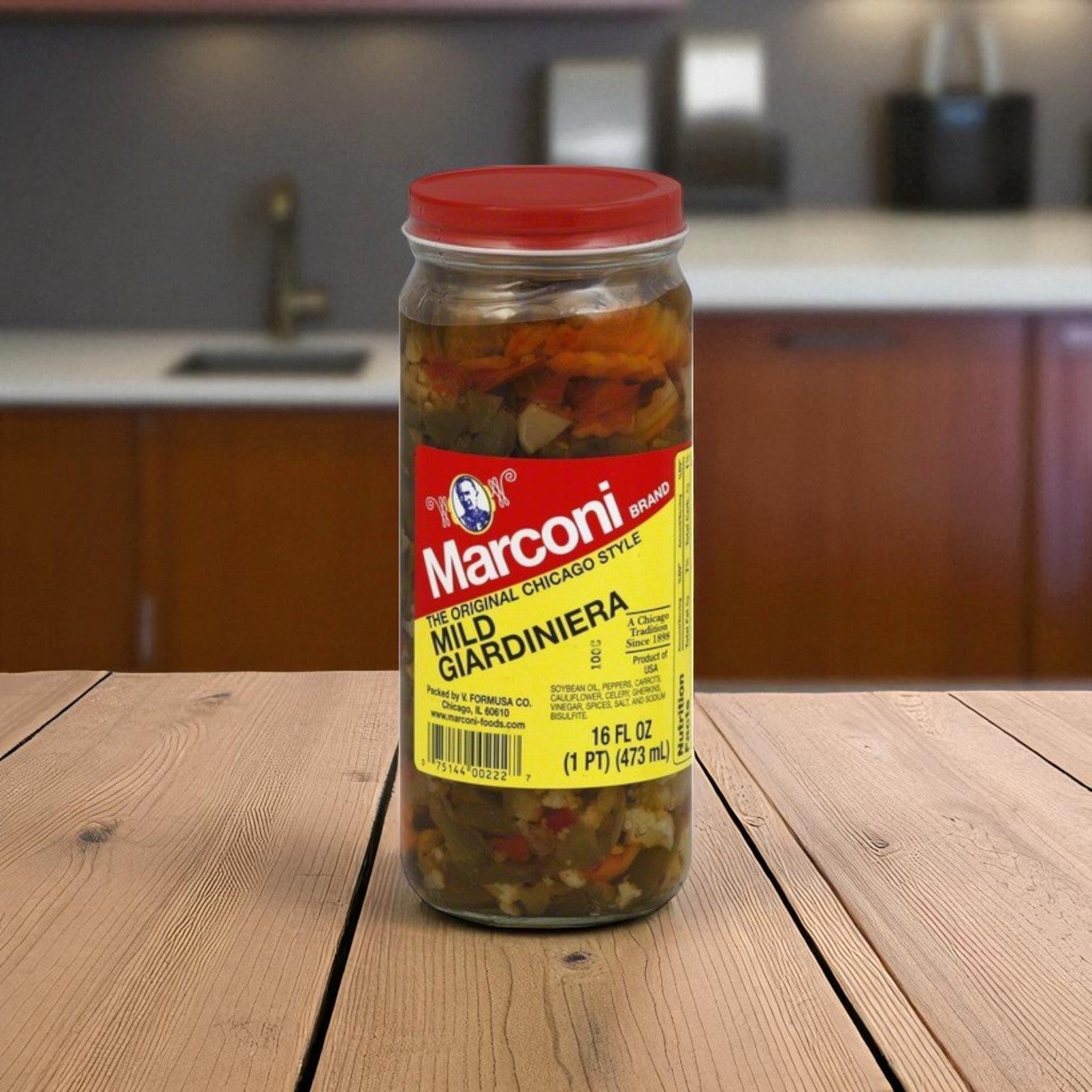 A 16 oz jar of Marconi Brand Giardiniera – Mild by Macroni Foods sits on a wooden surface in a kitchen, highlighting its authentic Chicago-style flavor.