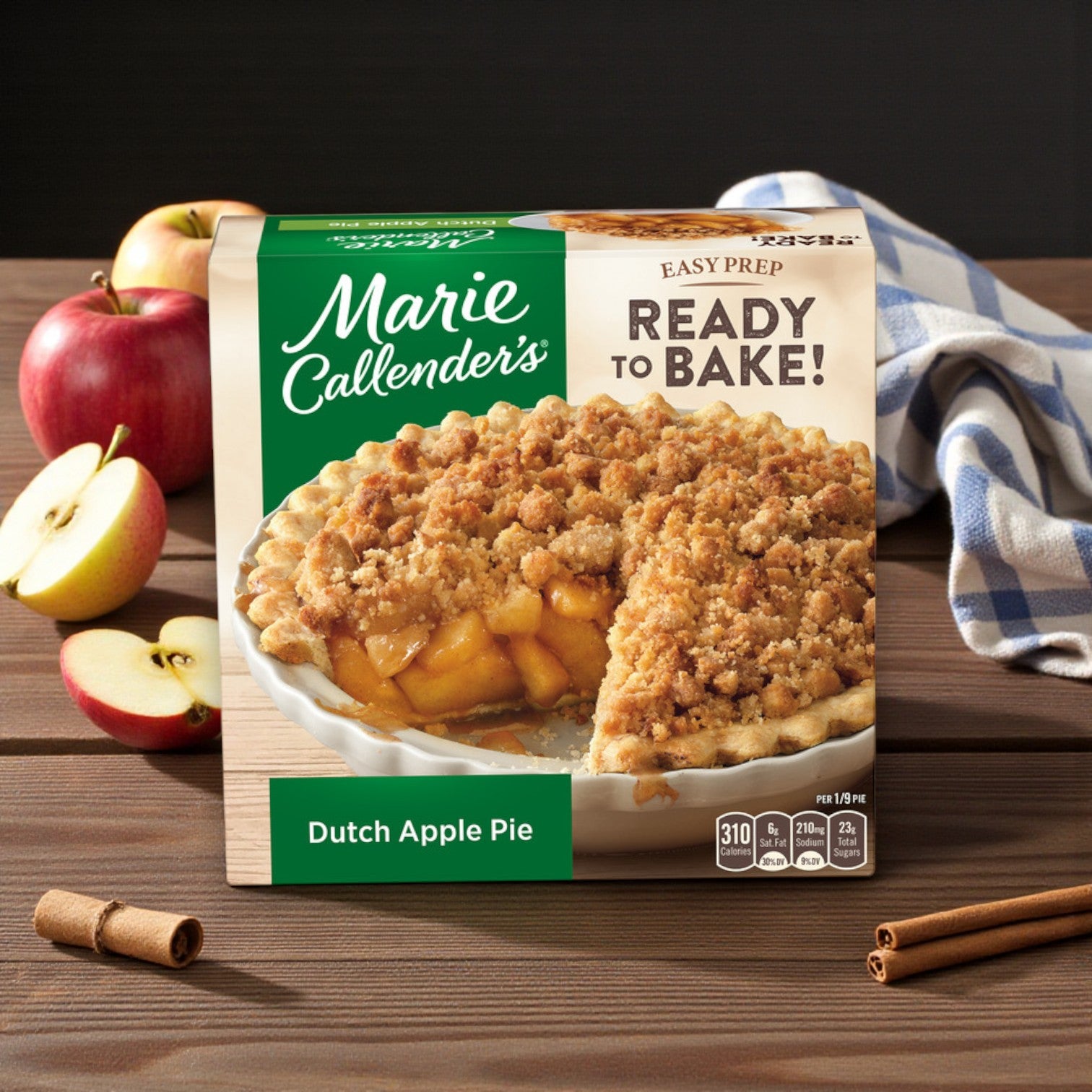 A 38 oz Marie Callender's Dutch Apple Pie – Ready to Bake Frozen Dessert box sits on a wooden table, surrounded by fresh apples and a striped cloth.