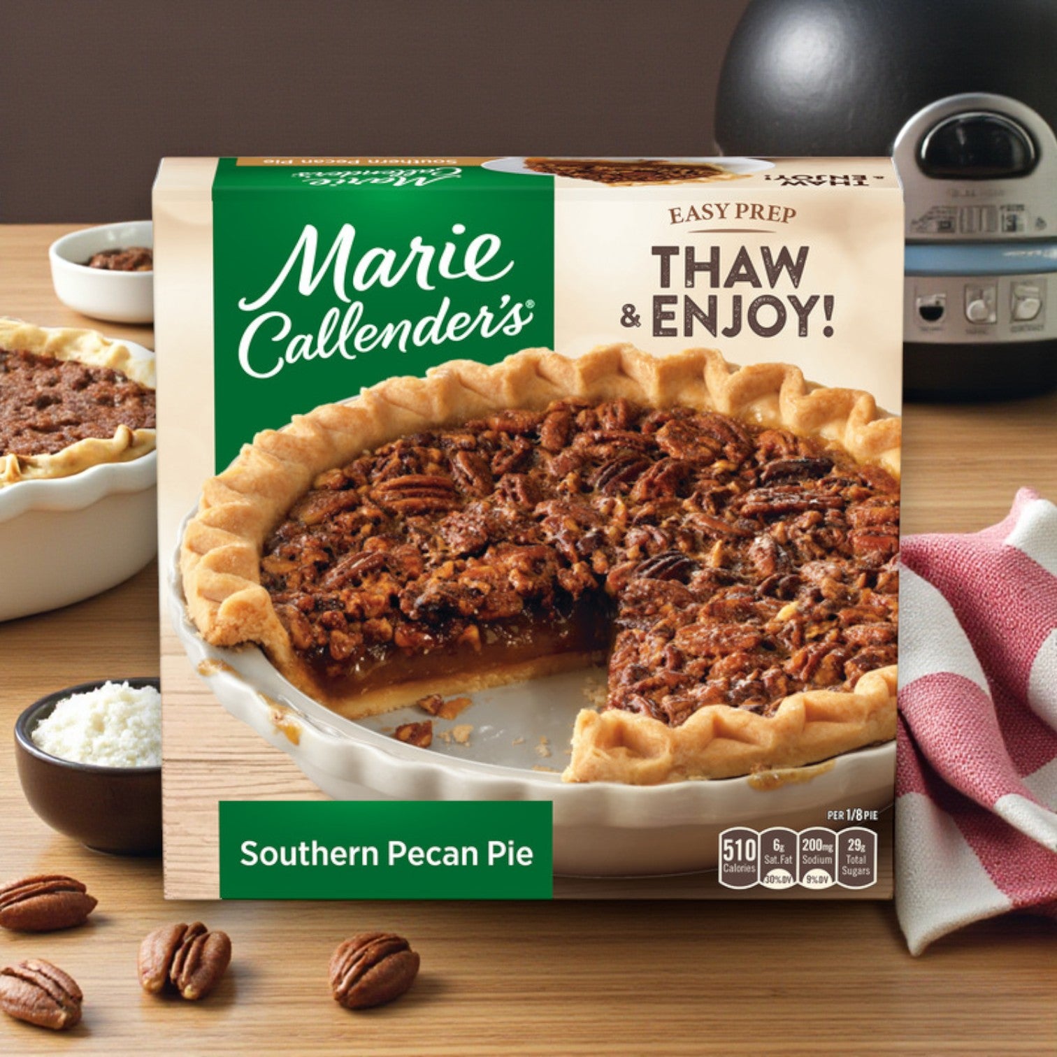 Marie Callender's Southern Pecan Pie – Frozen Dessert, 32 oz, is displayed with a slice removed in front of its packaging. Pecans, a striped napkin, and a small bowl of sugar are arranged nearby. Brand: Marie Callender's.