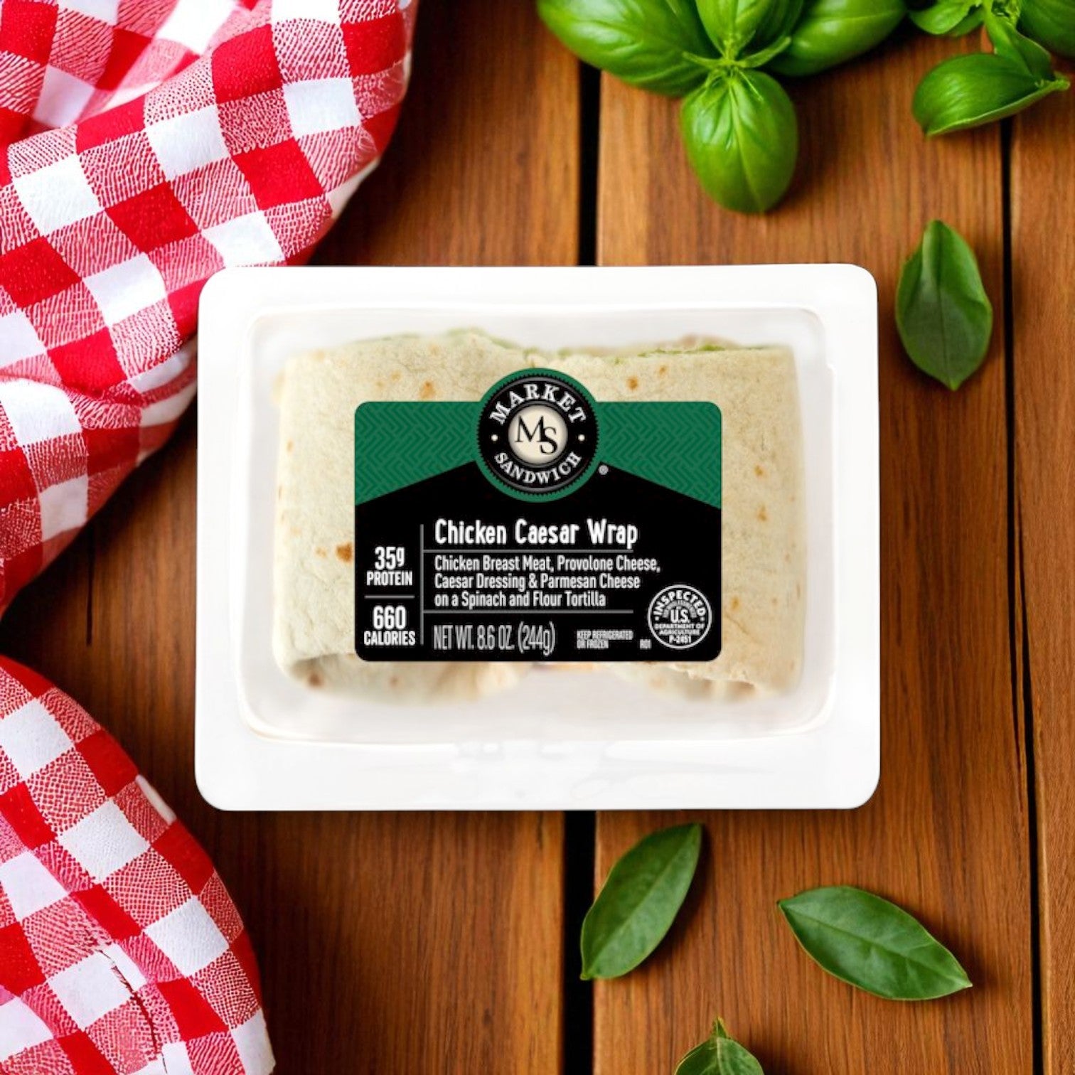 An E.A. Sween Market Wrap Combo Pack, featuring 4 Italian Style Wraps (8.2 oz) and 4 Chicken Caesar Wraps (8.6 oz), sits on a wooden table with fresh basil and a red and white checkered cloth nearby.