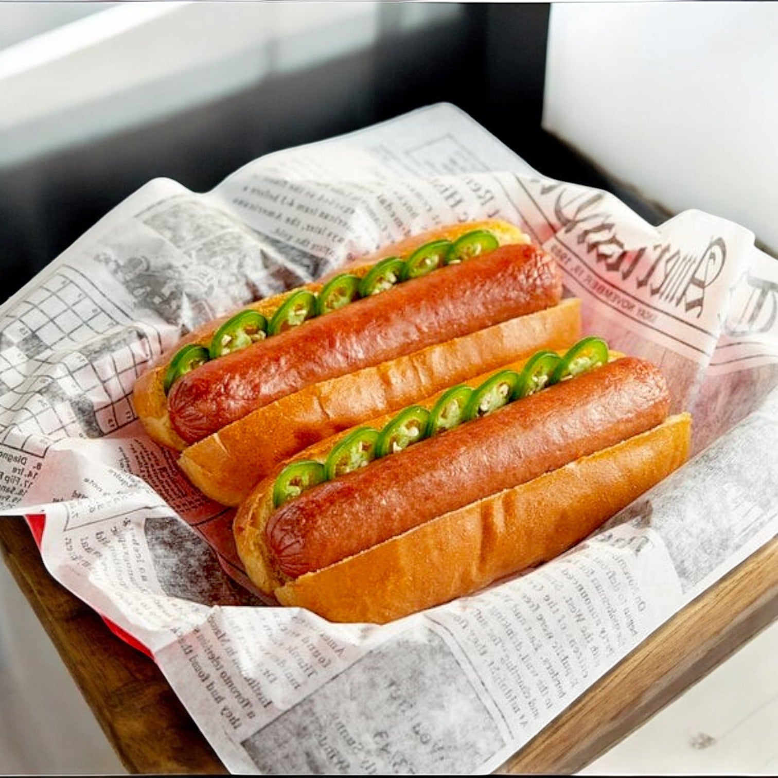 Enjoy two Colossal hot dogs made with Nathan's Famous Colossal Beef Franks from the 3 Family Packs (32 oz each, 24 hot dogs total), topped with sliced jalapeños and served on newspaper-style parchment in a wooden tray.