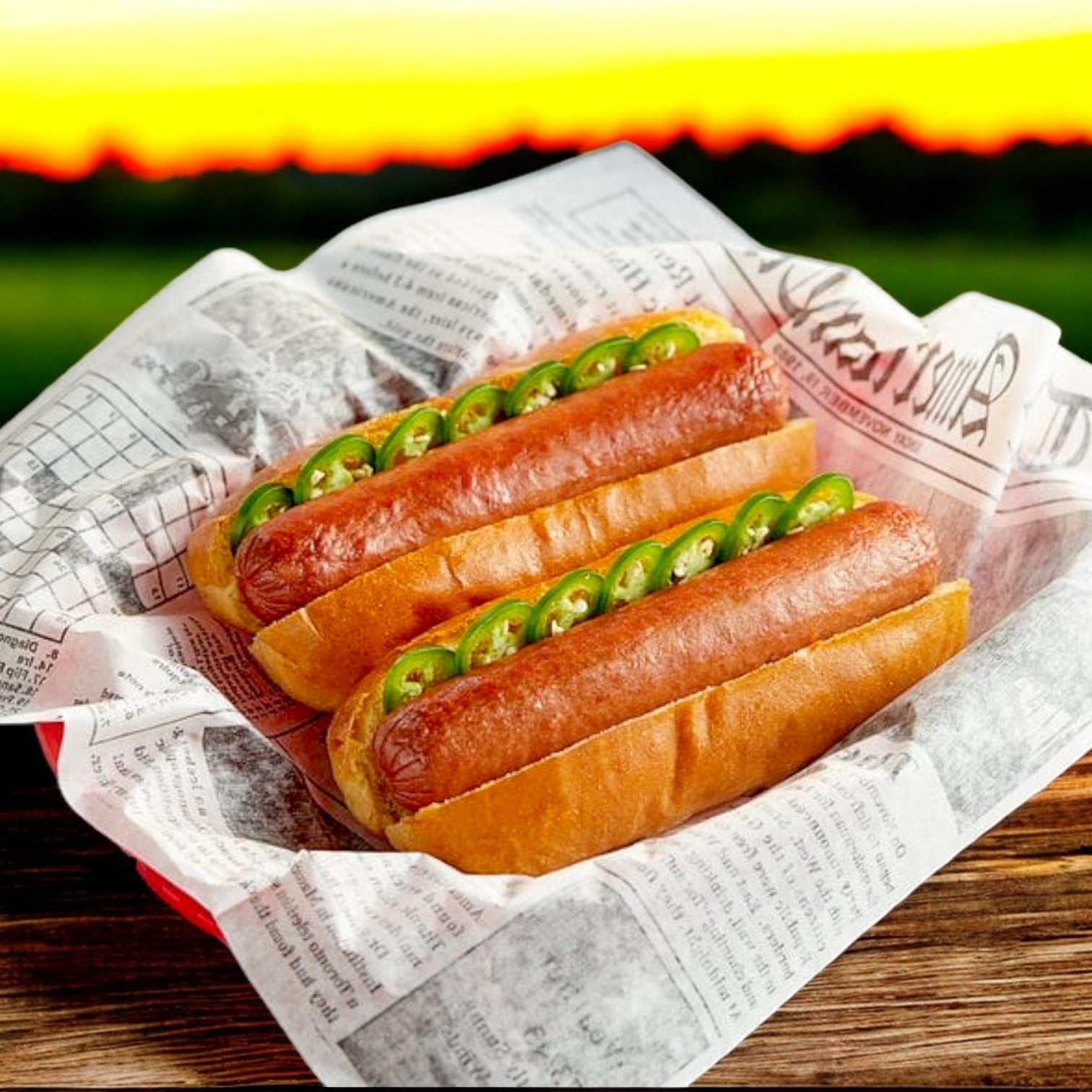 Enjoy two classic hot dogs made with Nathan's Famous Franks from the 12 oz pack, topped with sliced jalapeños and served in a basket lined with newspaper-style paper, set against a sunset and green field backdrop.