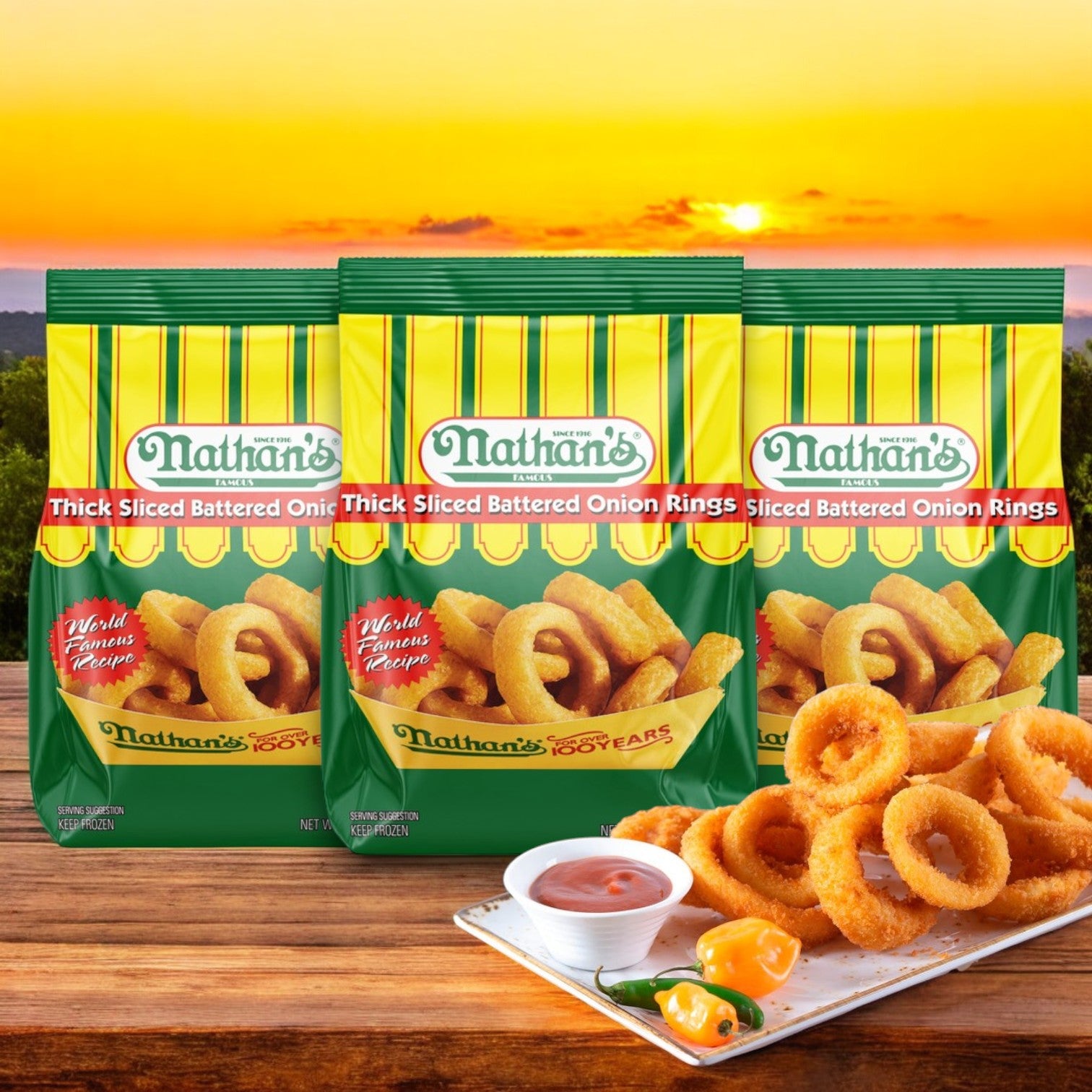 Three bags of Nathan’s Famous Thick-Sliced Battered Onion Rings (16 oz each) are shown before a sunset, with a plate of crispy onion rings, dipping sauce, and peppers in the foreground.