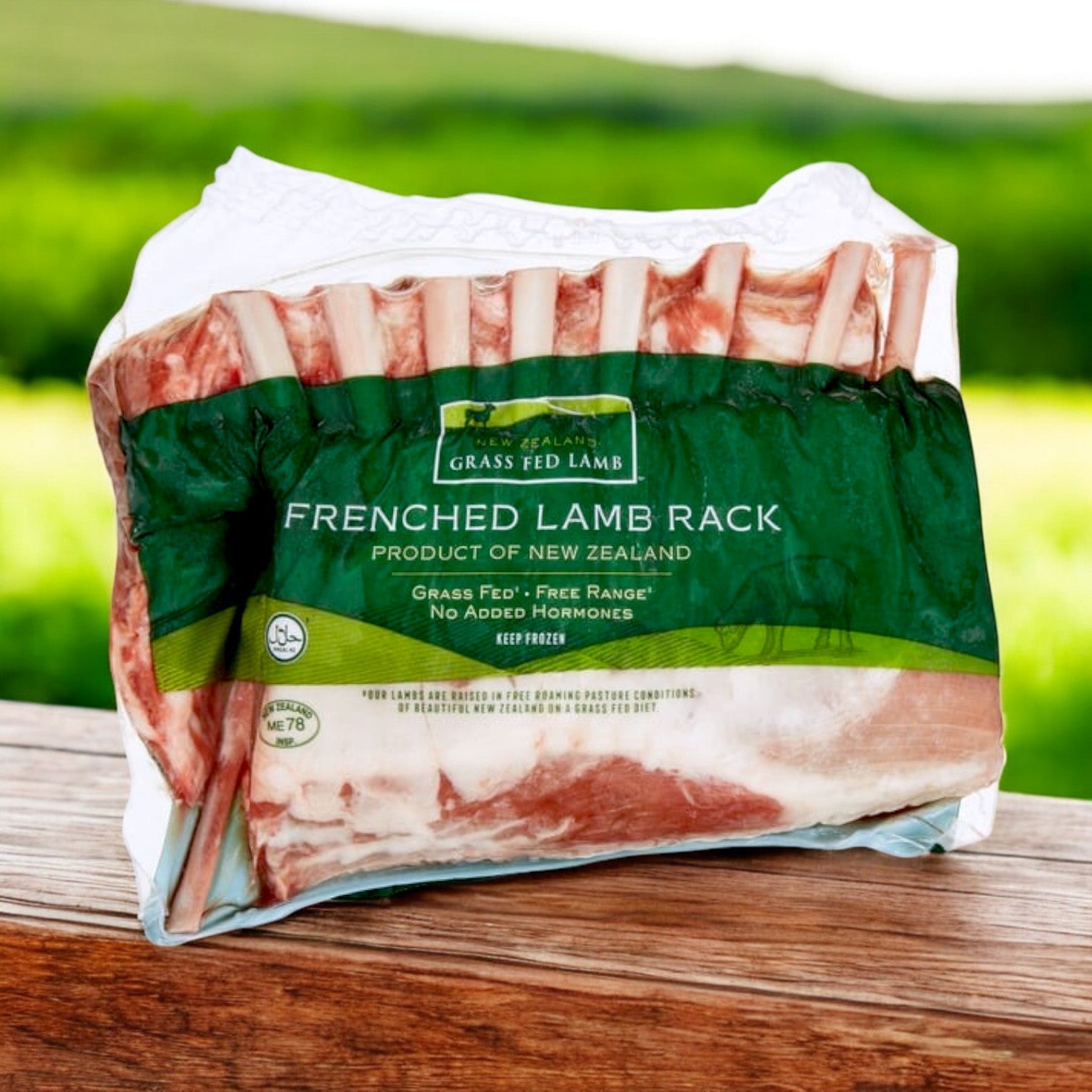 A New Zealand Spring Lamb Halal Frenched Lamb Rack, 3 lb avg, 2 per pack, rests on a wooden surface with a blurred green outdoor background.