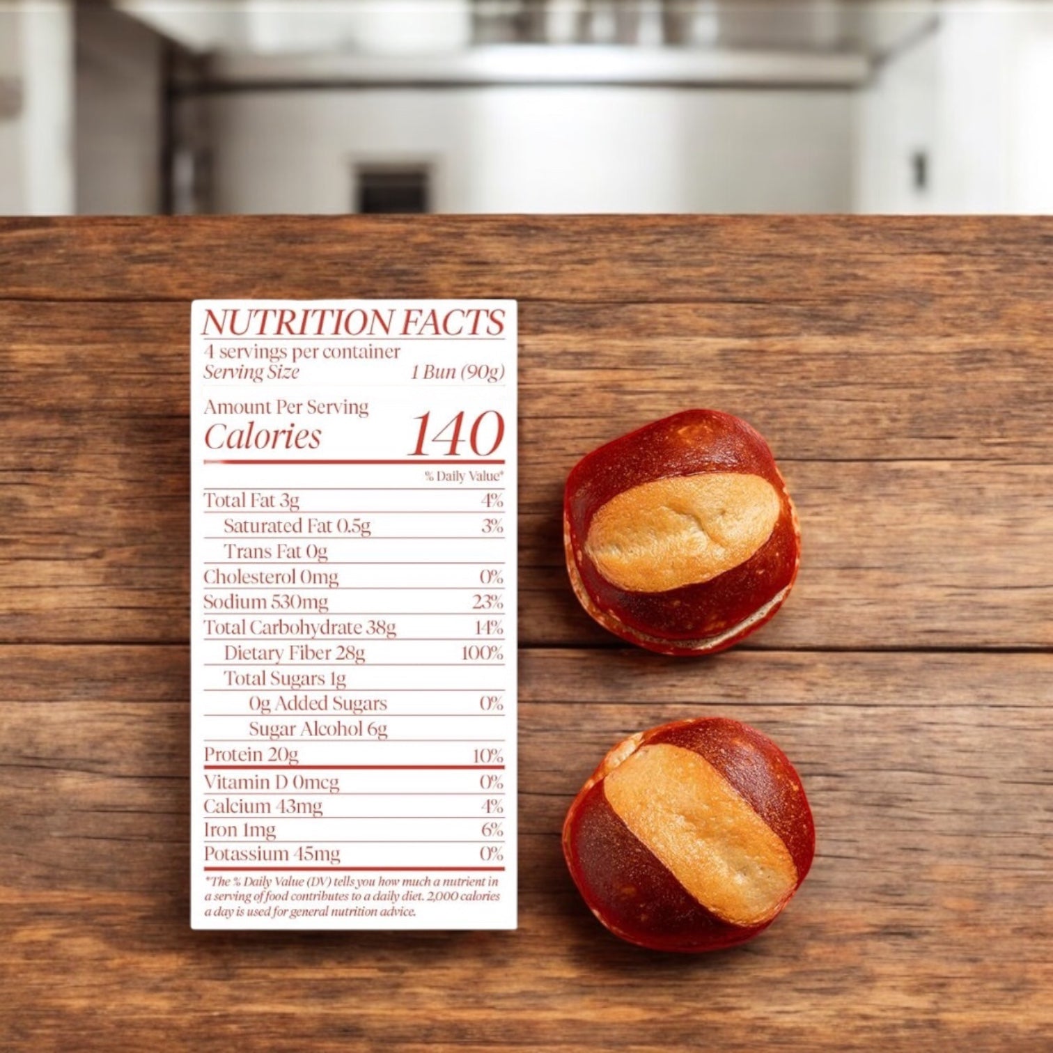 A nutrition facts label for BetterBrand, The Better Bun – Pretzel Style (140 calories) is shown next to two small buns on a wooden surface in a kitchen.