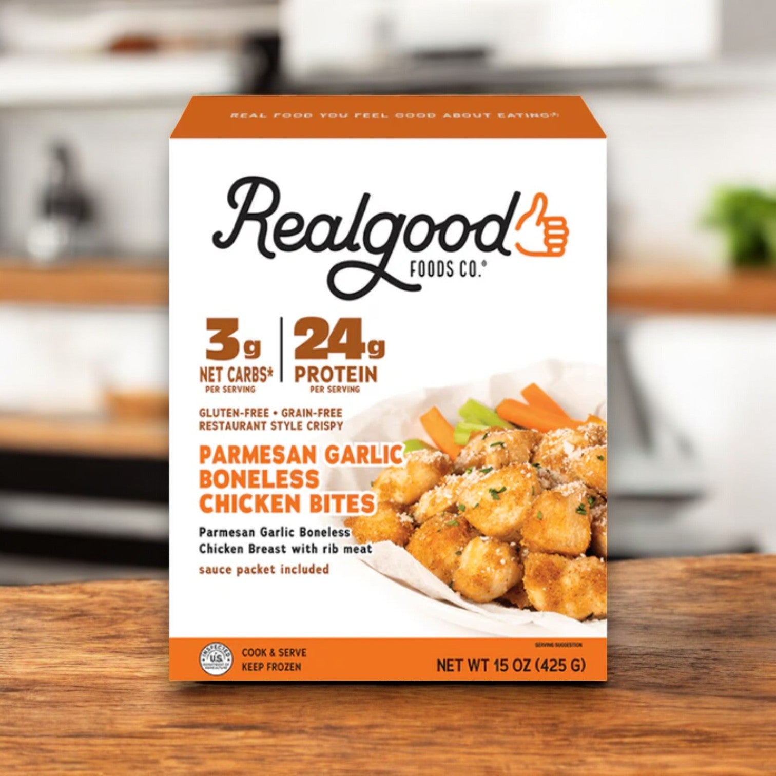 A box of Real Good Foods Low Carb Parmesan Garlic Boneless Chicken Bites (15 oz.), high-protein and gluten-free, sits on a wooden surface with nutrition facts and an image of the bites shown on the front.