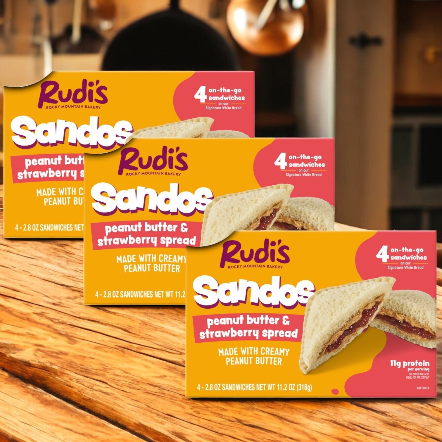 Three packs of Easy Lunches Rudi's Peanut Butter and Strawberry Spread Sandos (11.2 oz) are displayed on a wooden surface, highlighting this wholesome snack that's perfect for any time of day.