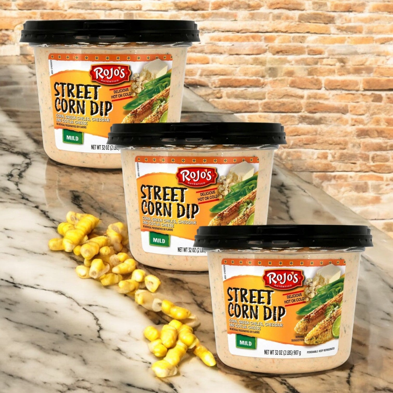 Rojo's Street Corn Dip—3 containers by Rojo's—are displayed on a marble surface with corn kernels, set against a brick wall background.
