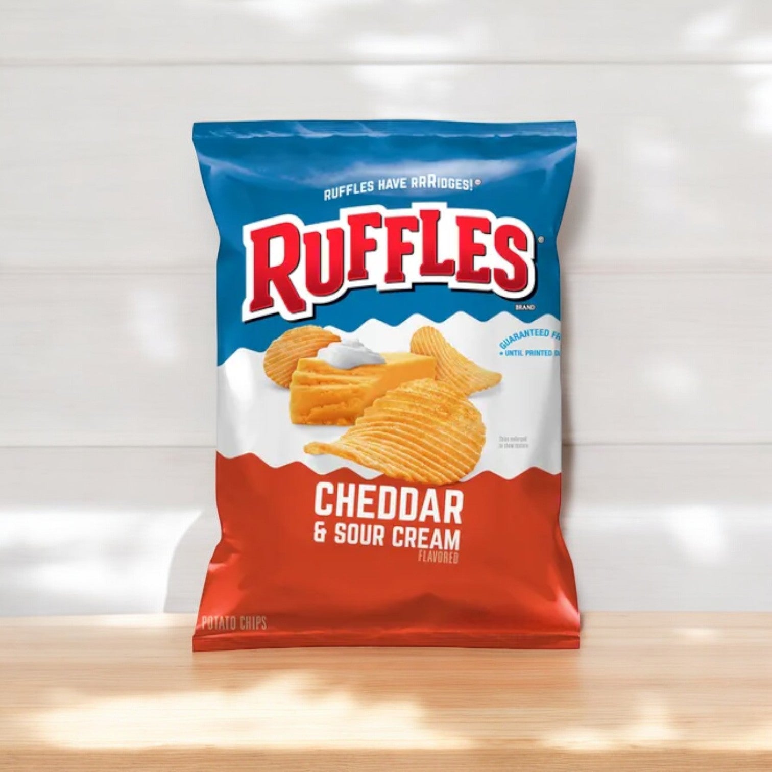 A pack of Ruffle's Potato Chips, Cheddar & Sour Cream Flavored (1 oz, 50 pk), rests on a wooden surface with a white background, ready to enjoy as a savory snack.