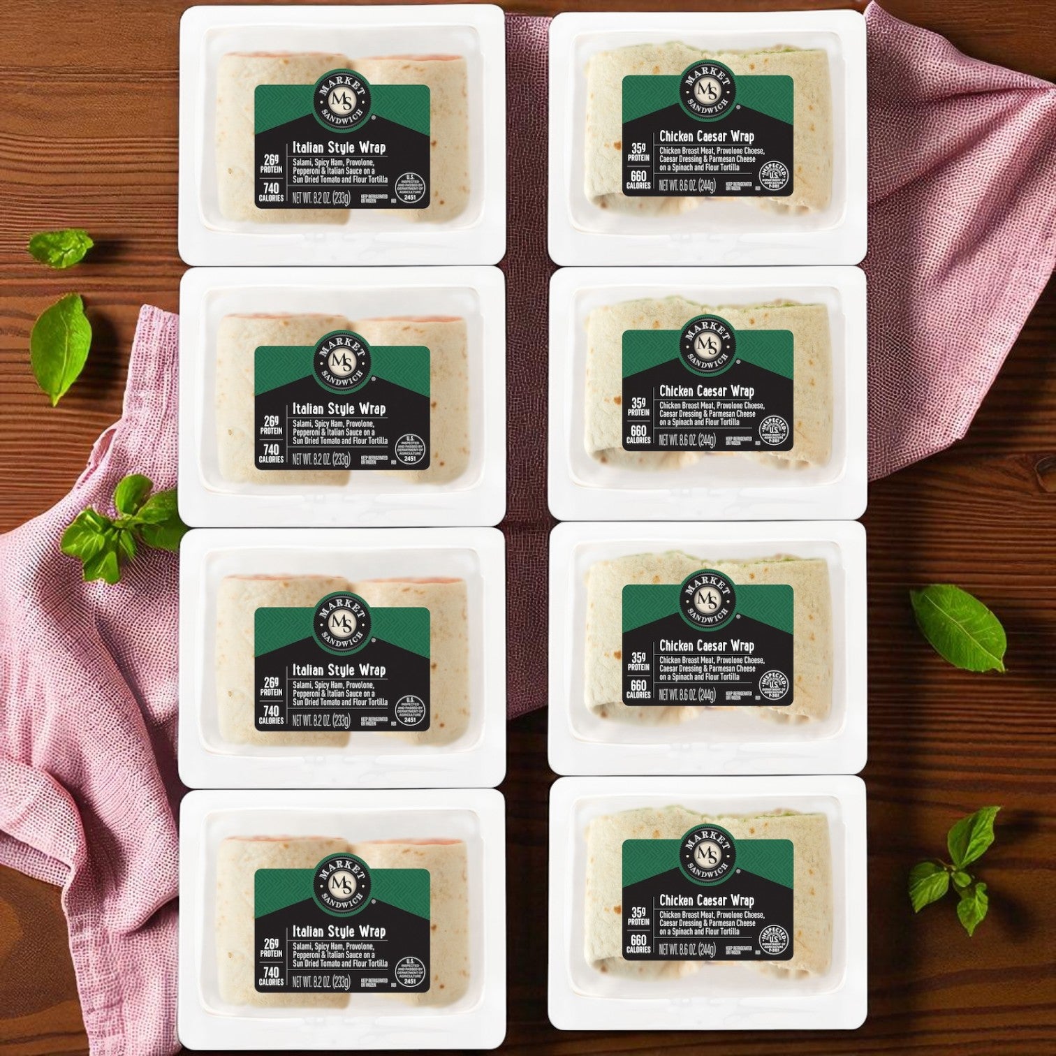 Eight E.A. Sween Market Wrap Combo Pack sandwiches—4 Italian Style (8.2 oz) and 4 Chicken Caesar (8.6 oz), each individually wrapped—are arranged in two rows on a dark wooden surface with a pink cloth and fresh green herbs.