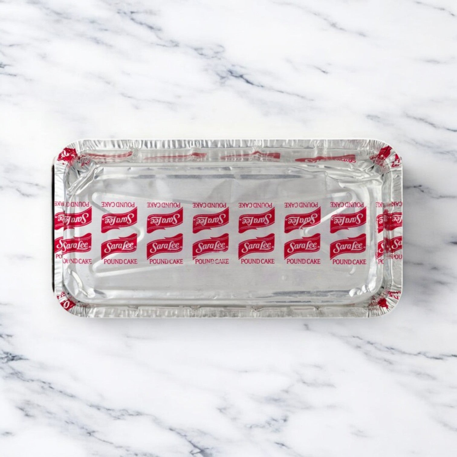 A rectangular Sarah Lee All Butter Pound Cake, 10.75 oz, from a 3 Pack sits on white marble, wrapped in branded foil—highlighting this classic dessert’s versatility for any occasion.