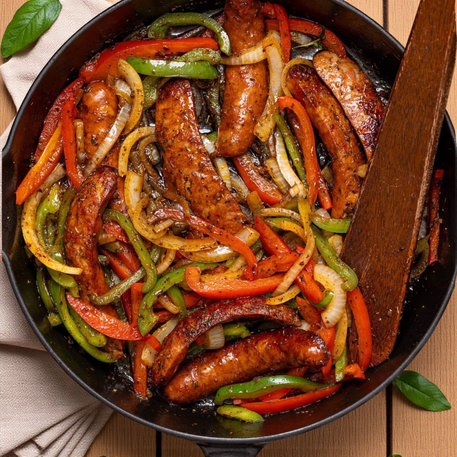 Johnsonville Andouille Sausage Links (4x1, 2/5 LB) from Johnsonville, sautéed with red and green bell peppers and onions in a skillet, deliver bold Southern flavor. A wooden spatula rests inside the pan.