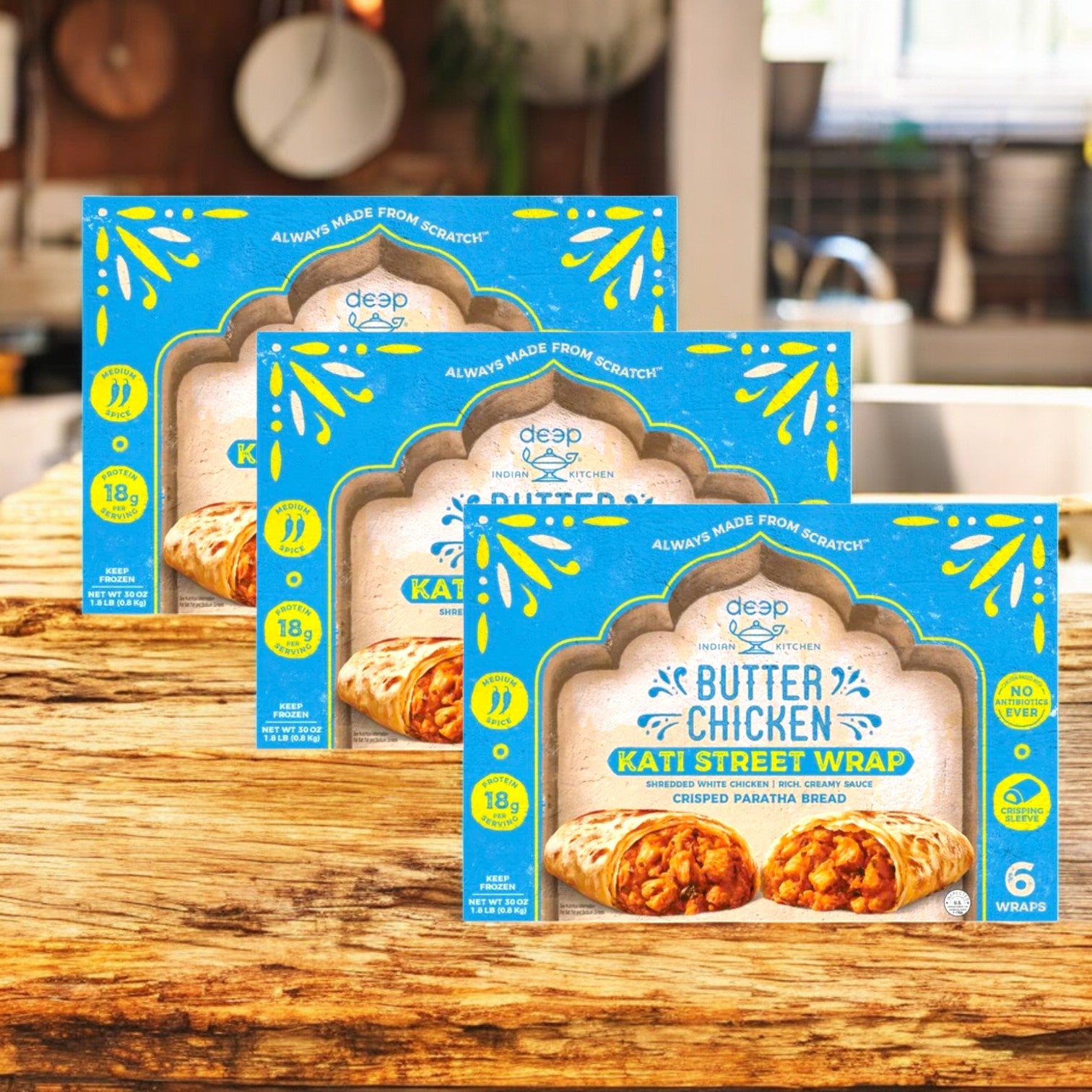 Three cases of Deep Indian Kitchen Kati Street Wrap, Butter Chicken, 6 count each, are displayed on a wooden surface in a kitchen setting.