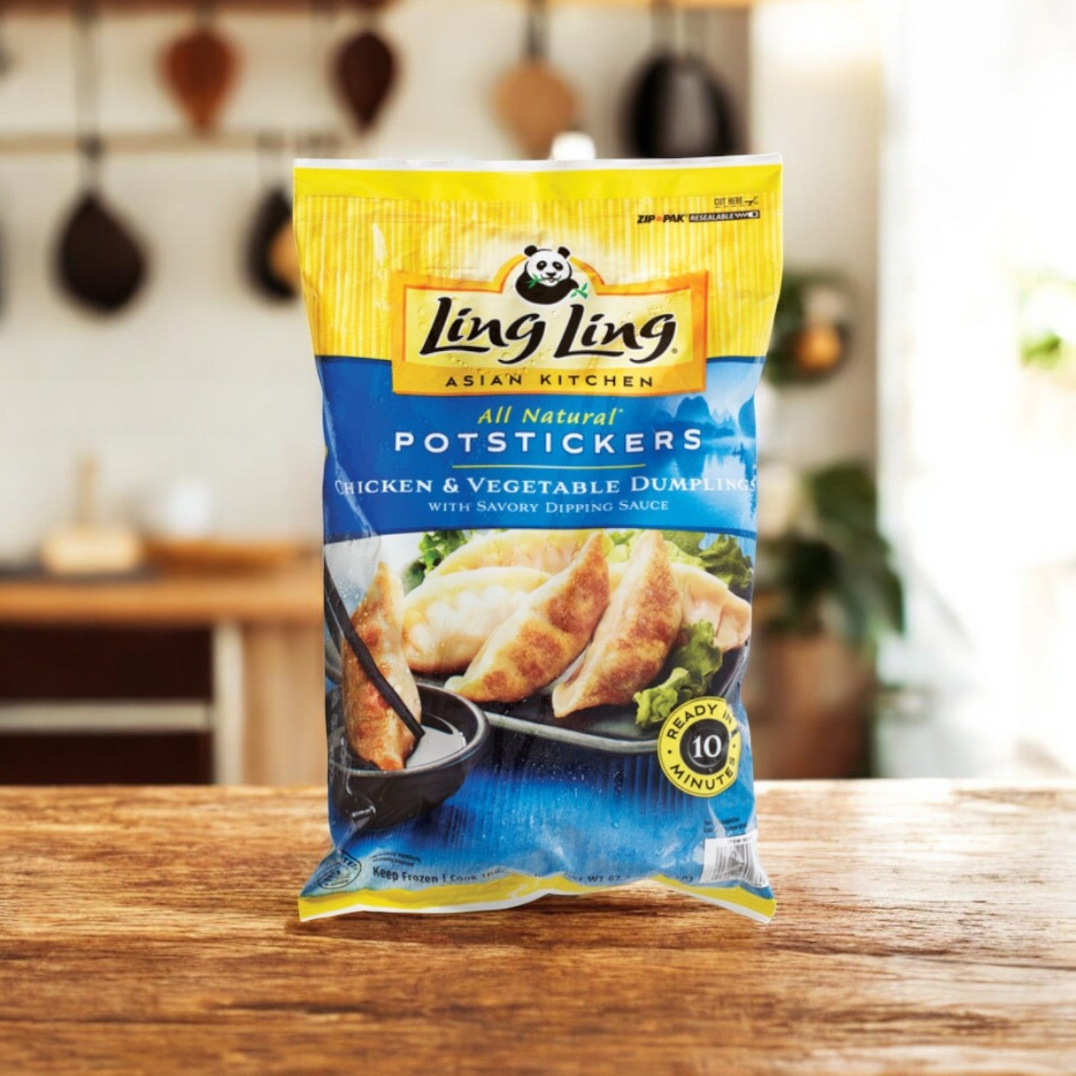 A pack of Ling Ling Potstickers, labeled "All Natural, Chicken & Vegetable," lays on a wooden table. The bag shows chicken potstickers on a black plate with dipping sauce.