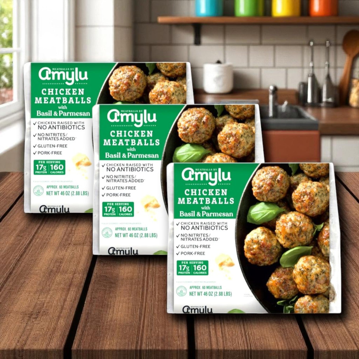Three boxes of Amylu ABF Chicken Meatballs with Parmesan & Basil, 46 oz-3 Count, are displayed on a wooden kitchen counter with a tiled backsplash and various utensils in the background.