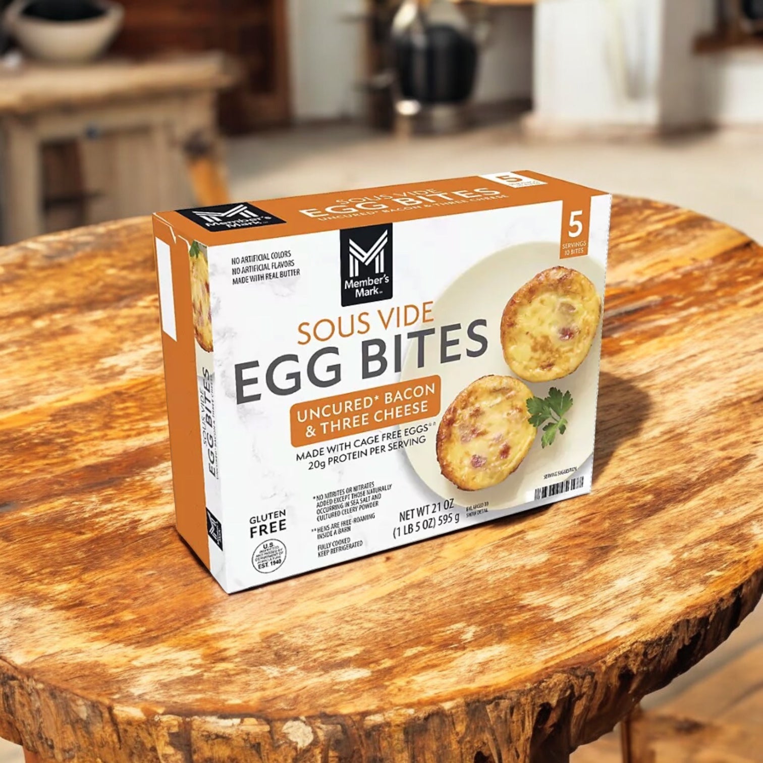A box of Easy Lunches Member’s Mark Sous Vide Uncured Bacon and Three Cheese Egg Bites sits on a wooden table against a rustic background.