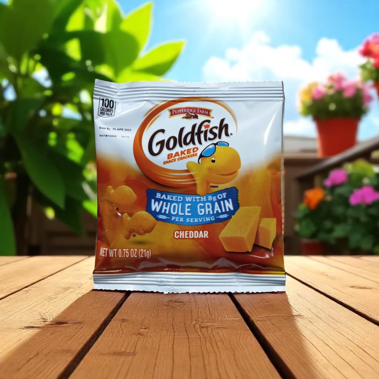 A bag of Easy Lunches Goldfish Whole Grain Cheddar Crackers, .75 oz., is displayed on a wooden table outside with plants and flowers in the background, offering a wholesome snack made with real cheddar cheese.