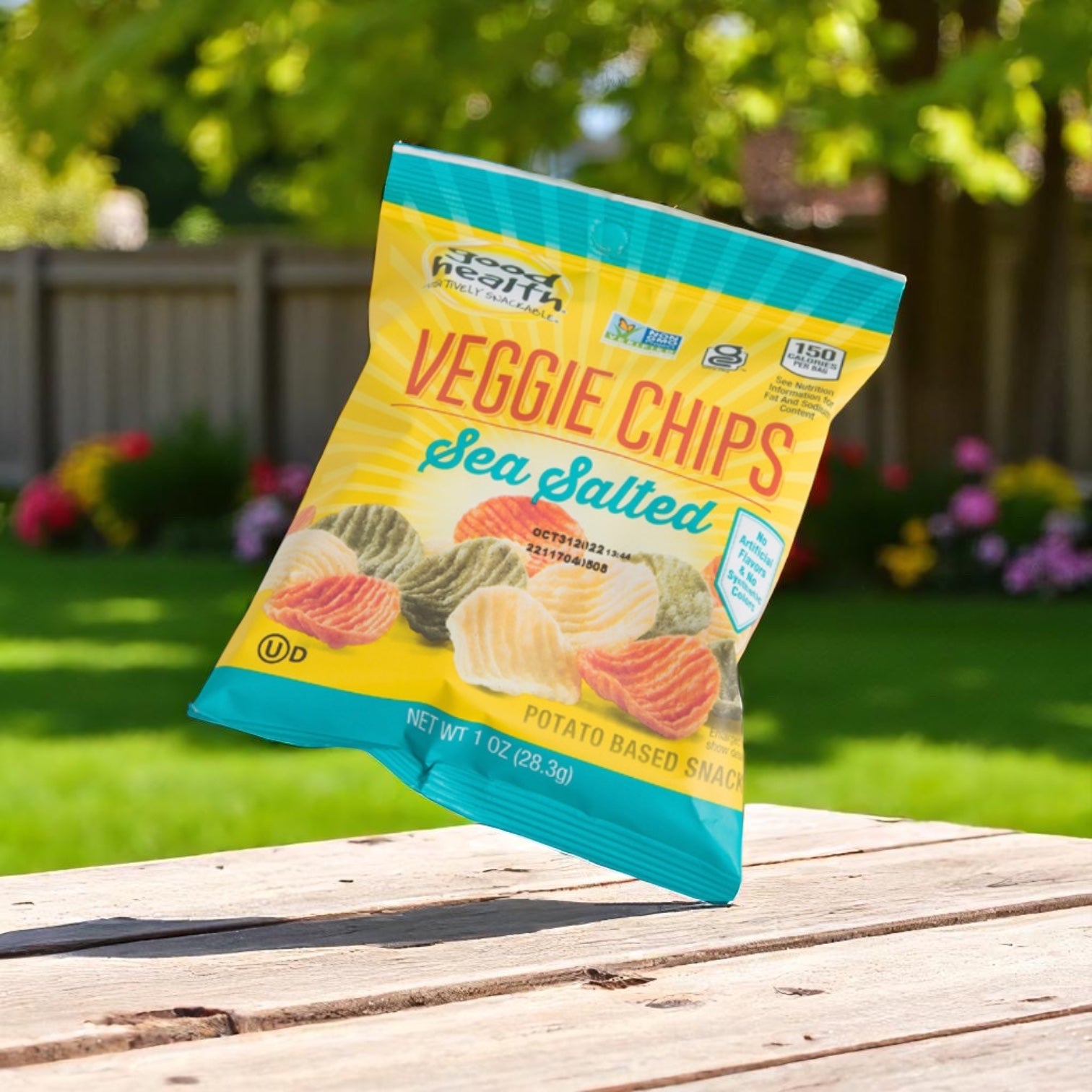 A bag of Easy Lunches Good Health Vegetable Chip Snack, 1 oz., from a 24-count case, is on a wooden table outdoors with a blurred green garden and flowers in the background.